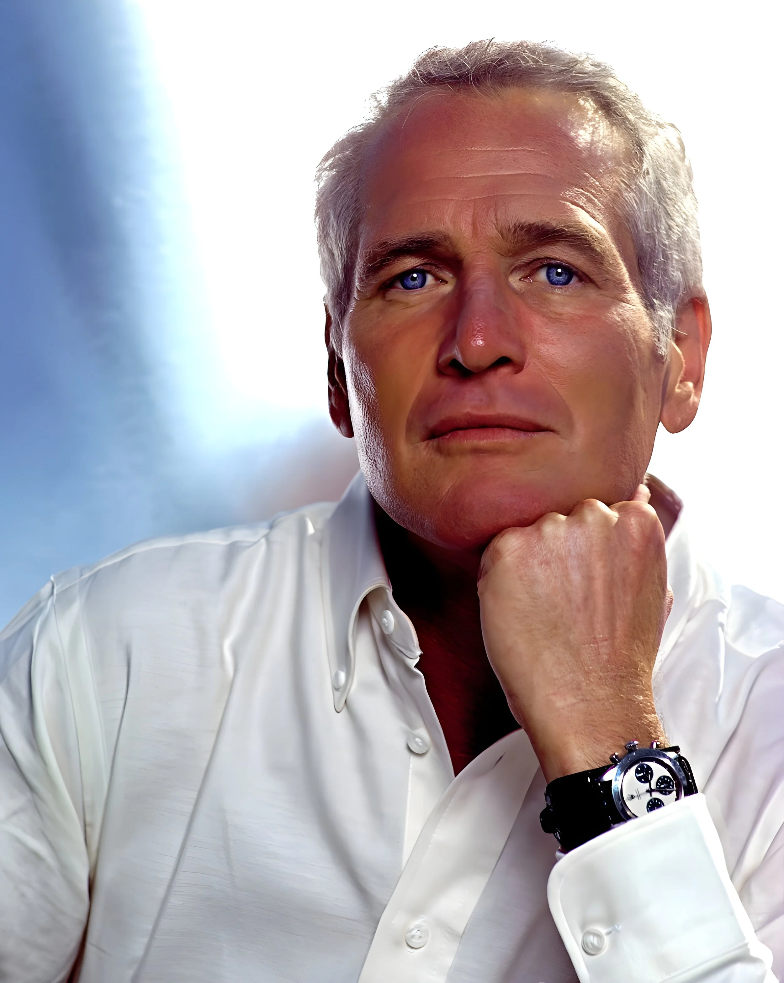 A middle-aged man with gray hair and blue eyes wearing a white dress shirt and a watch on his left wrist, resting his chin on his hand and looking into the camera.