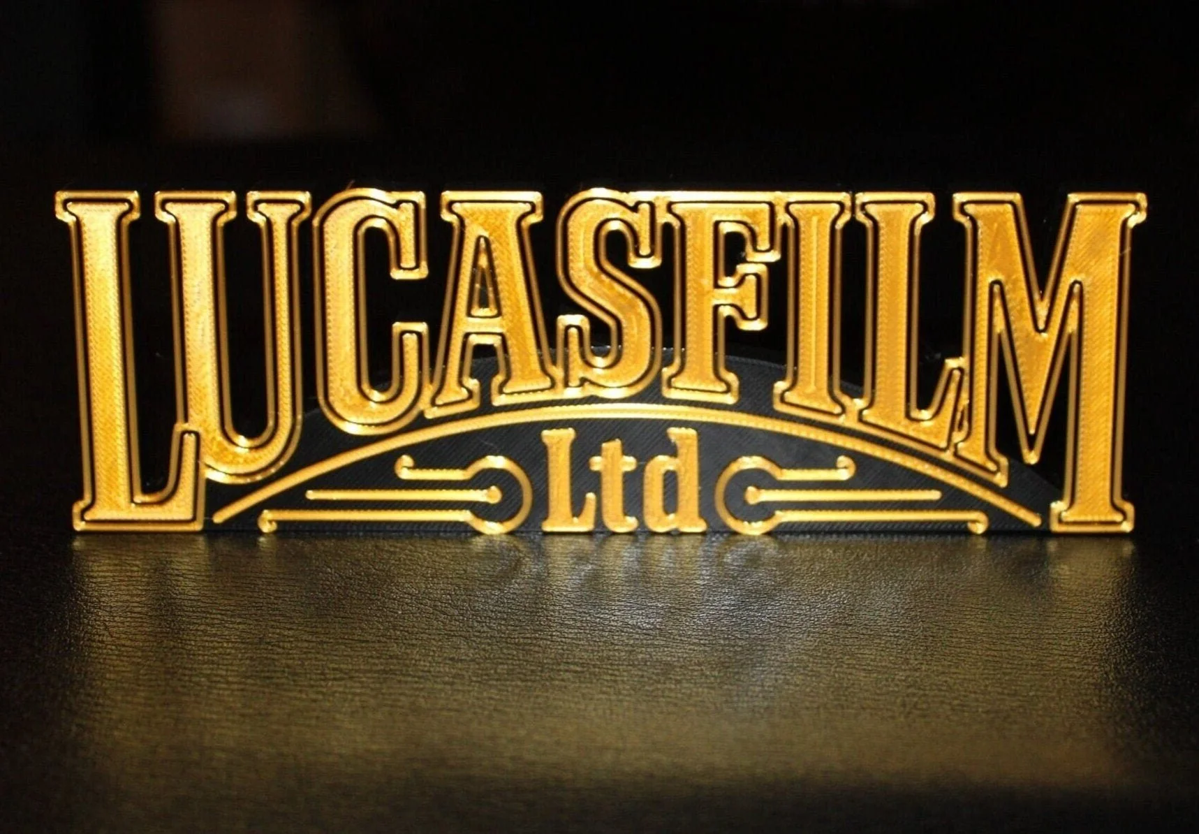 Backlit illuminated sign with the words 'LUCASFIM Ltd' in large gold letters and a decorative flourish underneath.