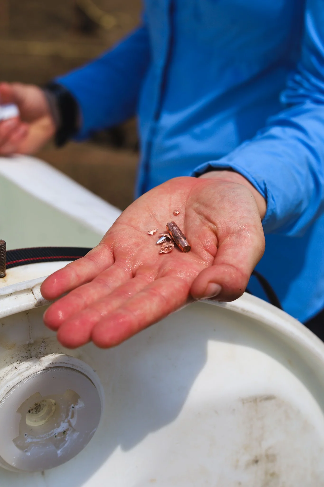 A person in a blue jacket holding an expanded copper bullet.