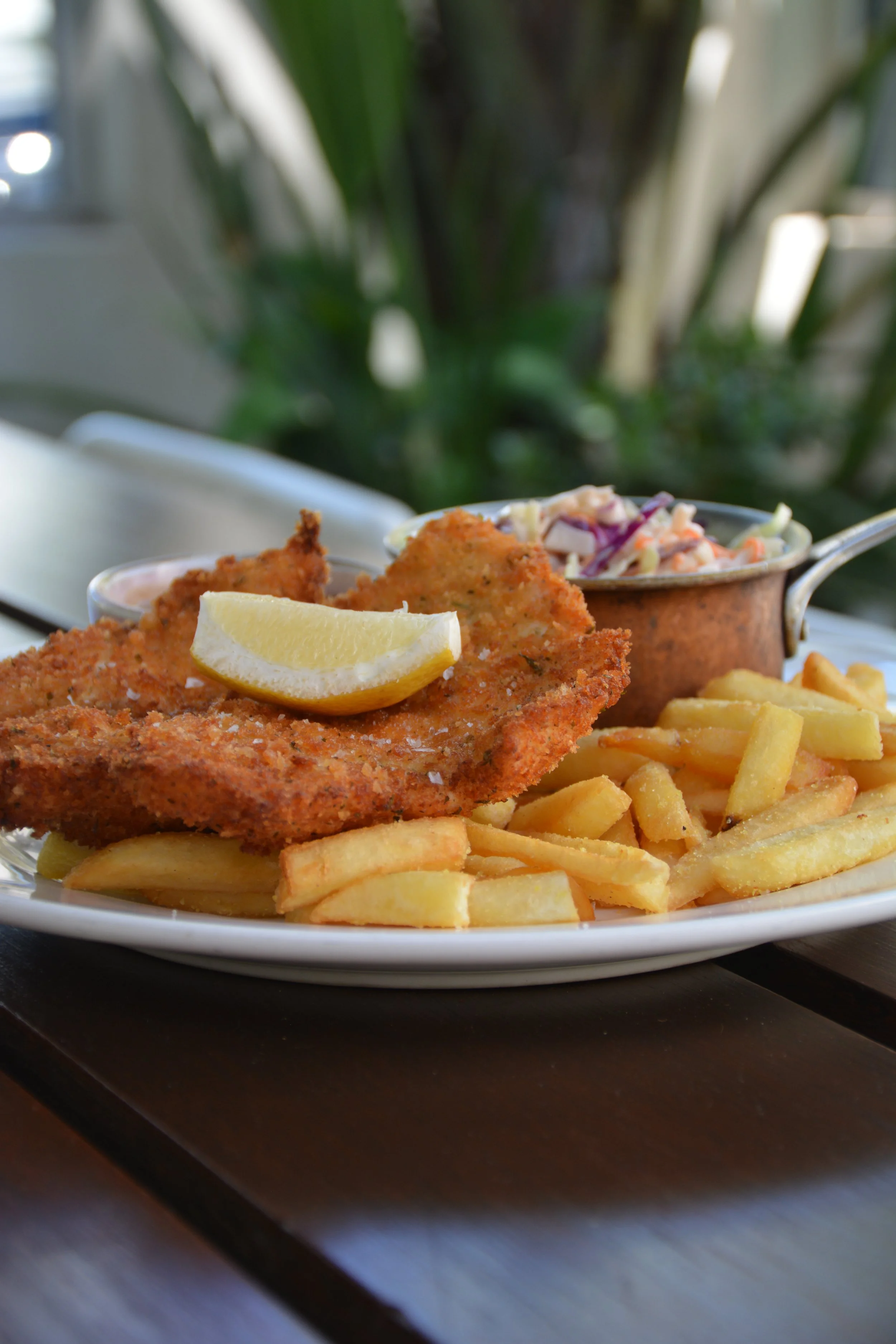 Fried fish fillet with a lemon wedge, served with French fries and coleslaw, on a white plate.