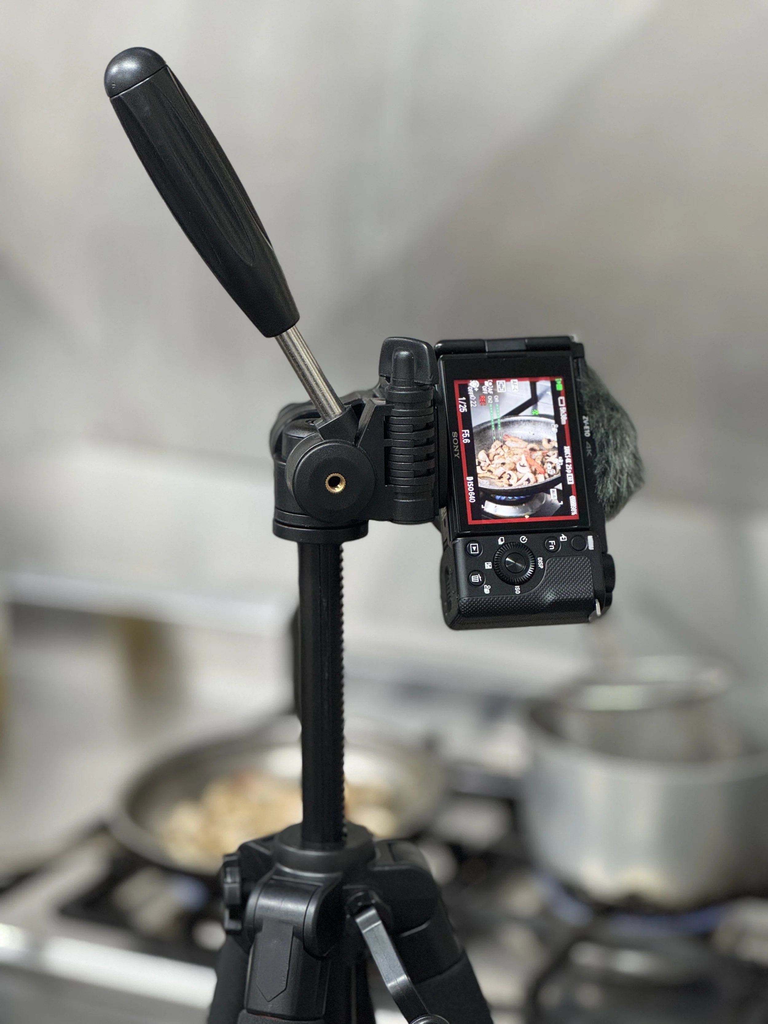 A camera mounted on a tripod capturing a close-up view of a stove with a pan of food cooking.