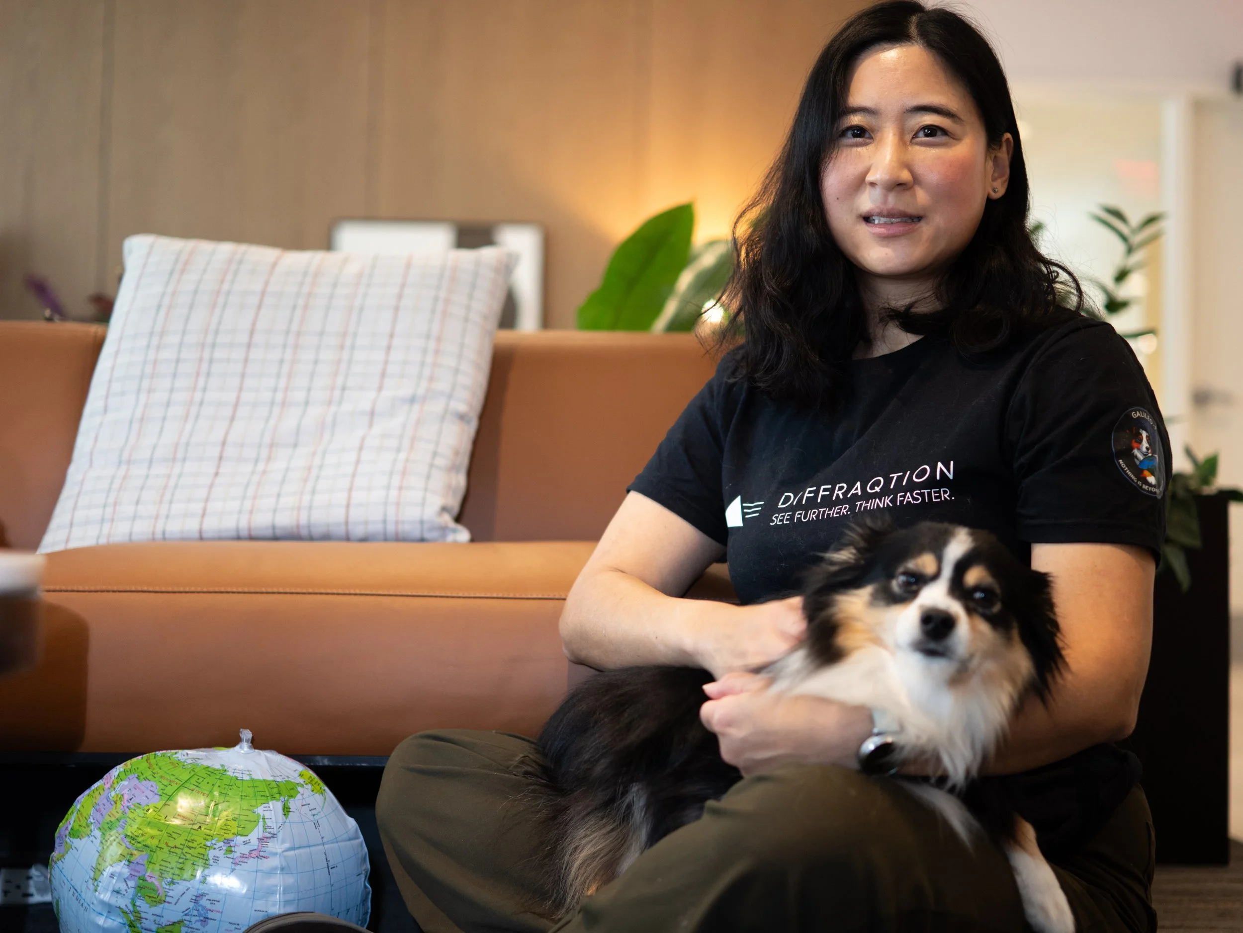 Headshot of a woman with long black hair wearing a dark blazer and maroon blouse, smiling at the camera against a gray background.