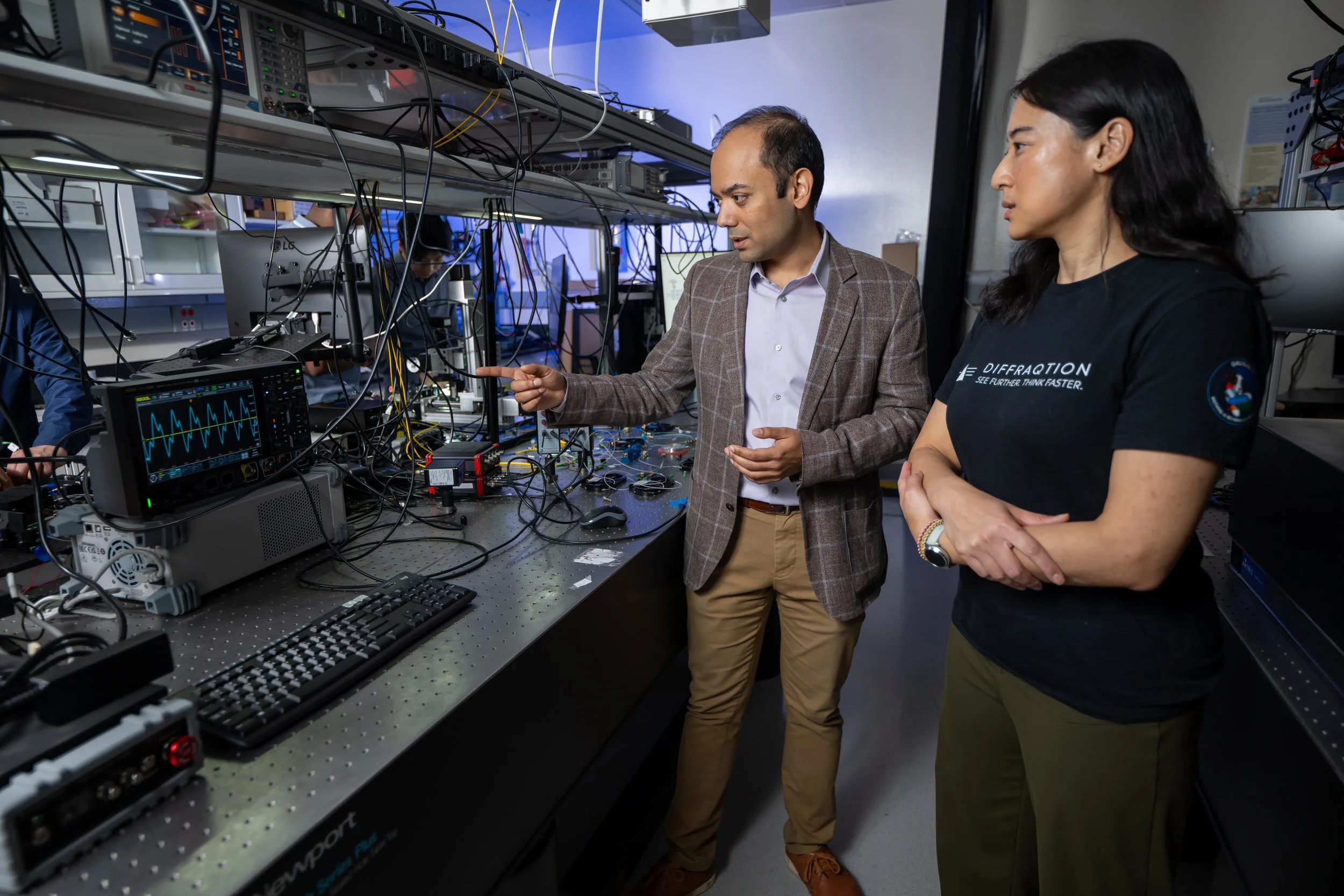 Three men working with electronic equipment, oscilloscopes, and monitors in a dark room, possibly conducting experiments or tests.
