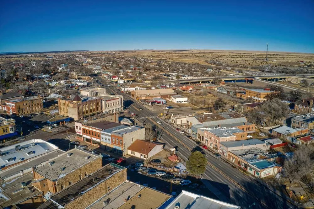 Aerial view of a small town with downtown area, streets, buildings, and some open land in the background under a clear blue sky.