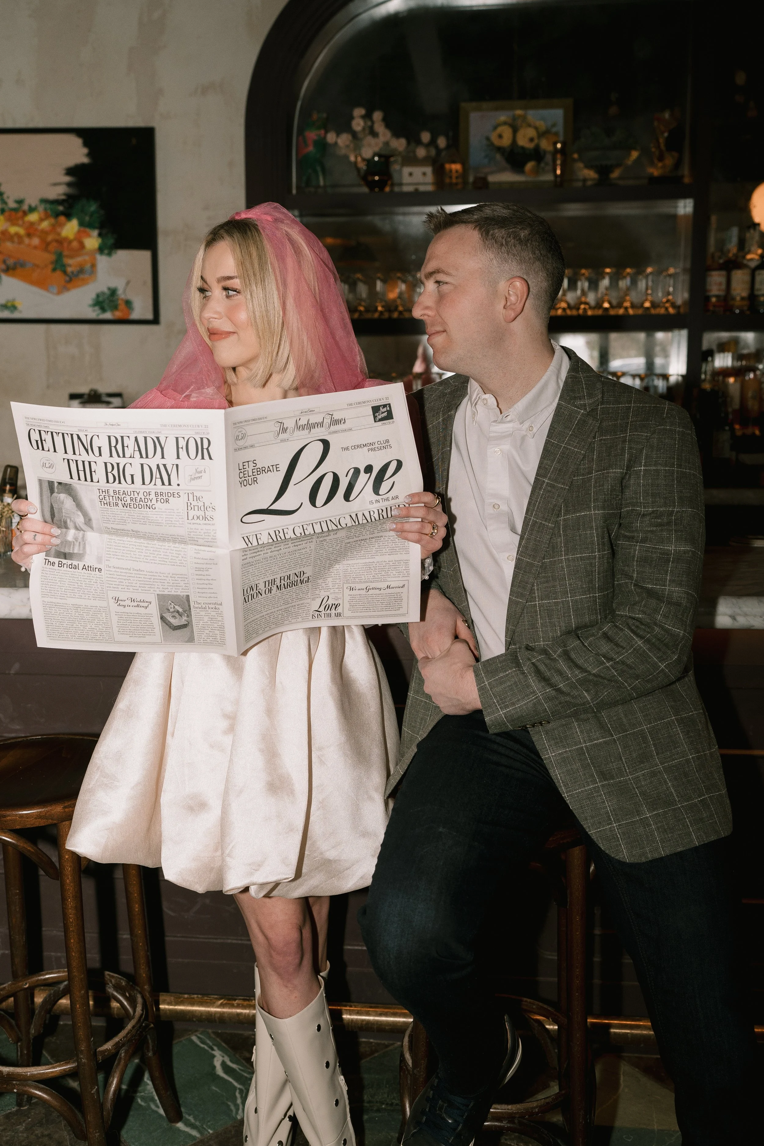 woman holding a newspaper announcing her engagement - she looks off to the side while he looks at her