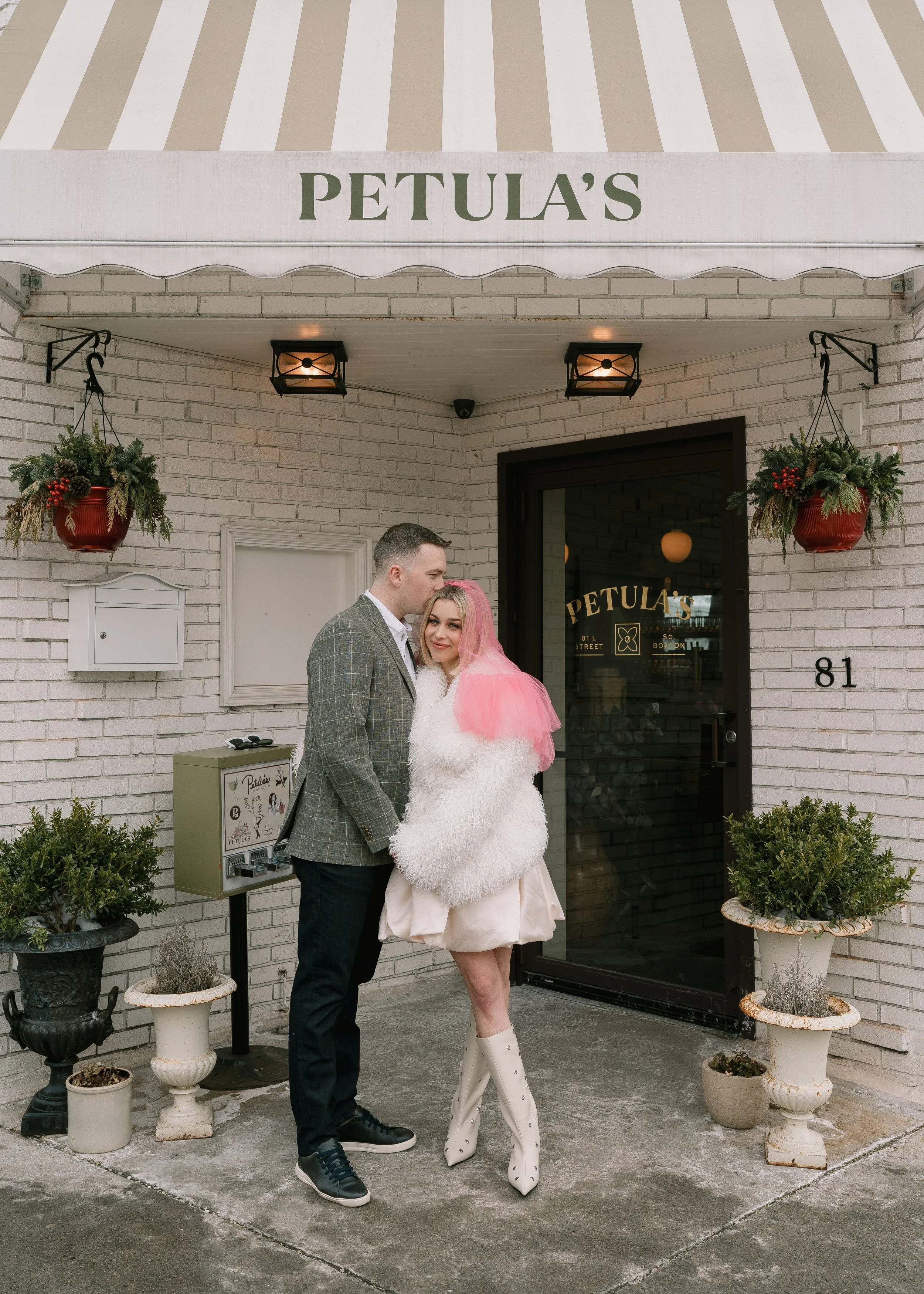 couple holding hands and standing in front of the restaurant in an editorial fashion - the woman wears a pink veil and vintage, chich accessories for this engagement photoshoot in Boston.