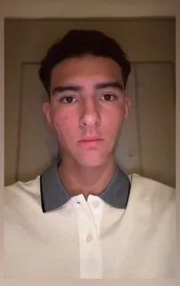 A young man with dark hair and fair skin, wearing a white polo shirt with a gray collar, looking directly at the camera.