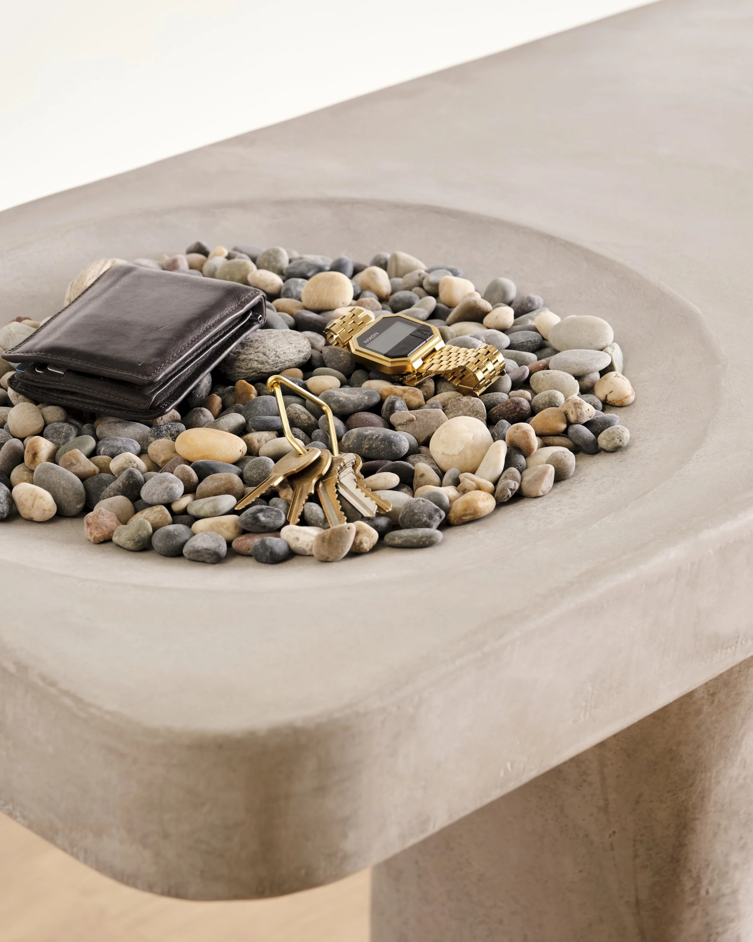 Detail of Pebbles Entry Table's hand-sculpted surface with built in catch-all dish that has been styled with pebbles, a wallet, and keys. 