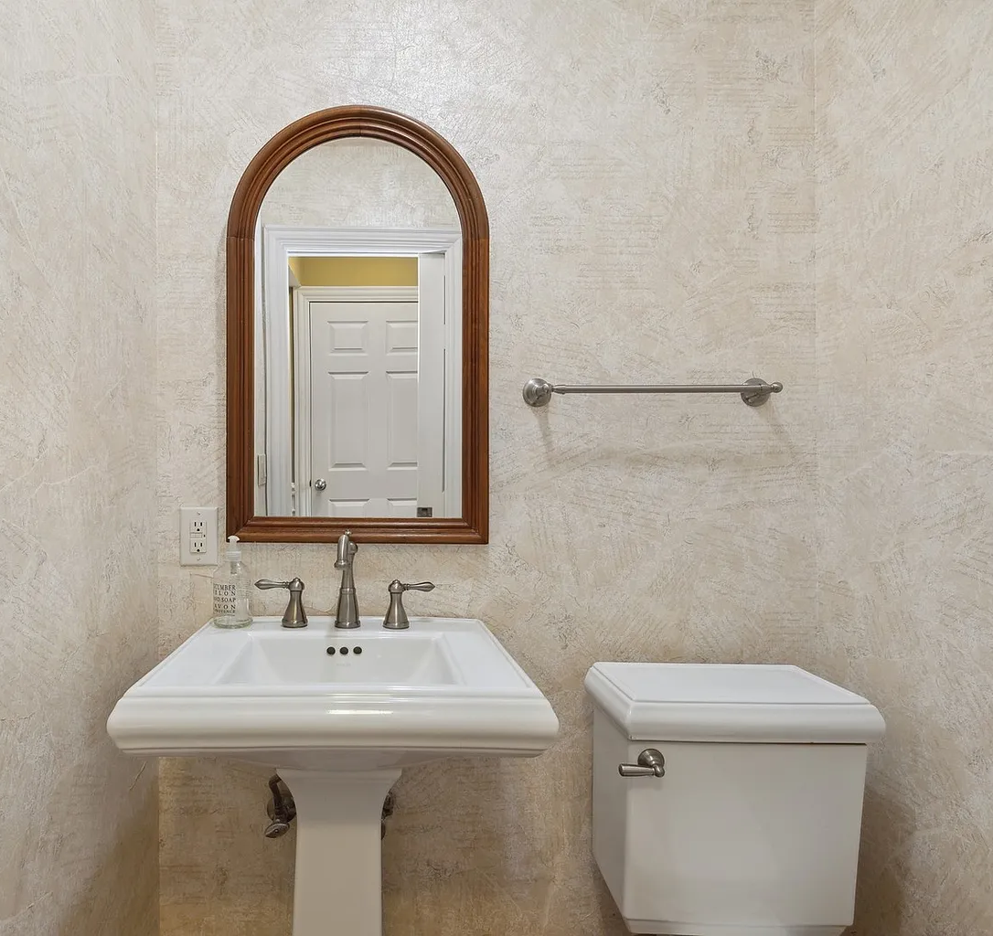 Bathroom with pedestal sink, mirror, toilet, and empty towel rack on beige wall.