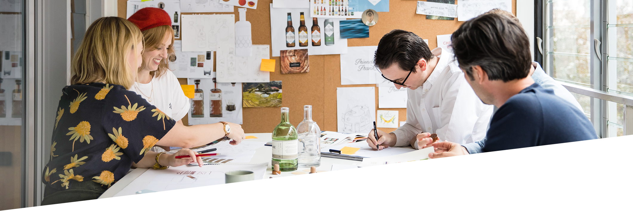 Group of four people working together at a table, surrounded by sketches and design materials, in a creative office setting.