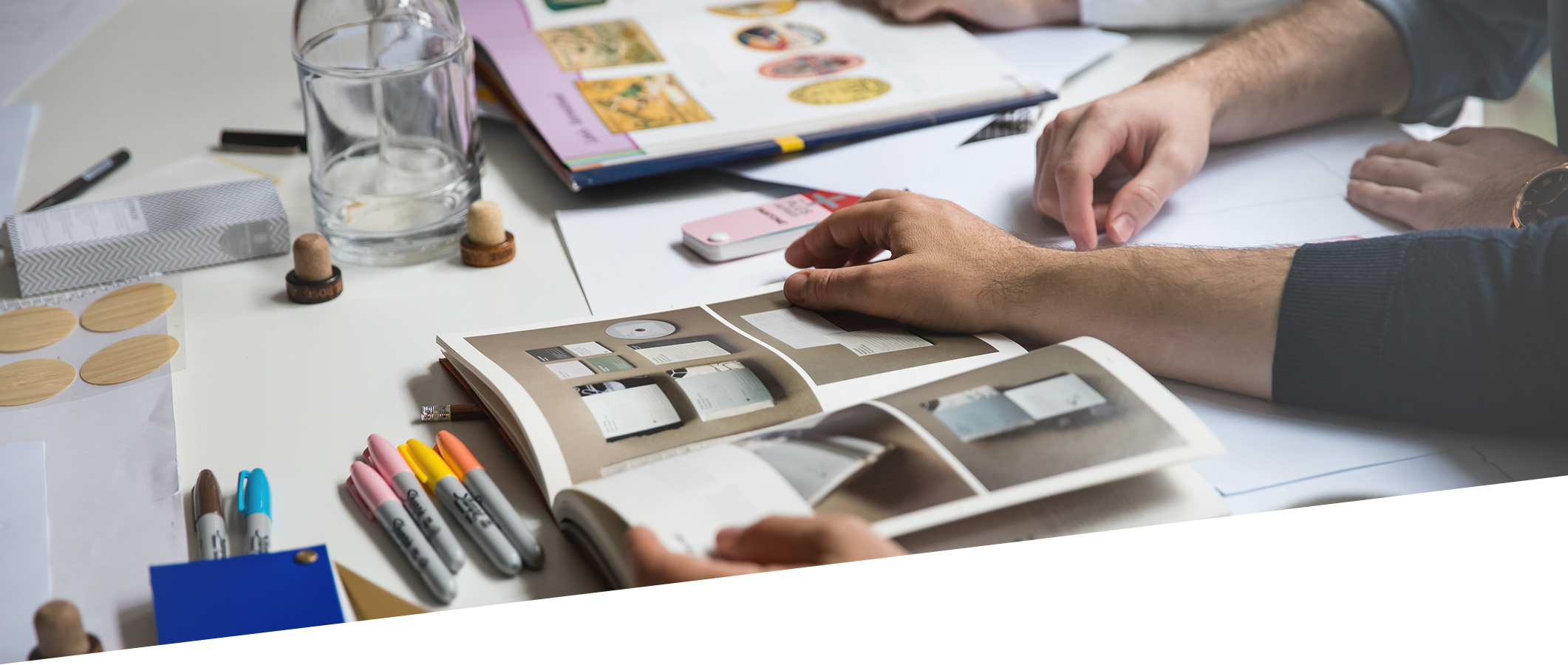 People working at a table with design books and colored markers.