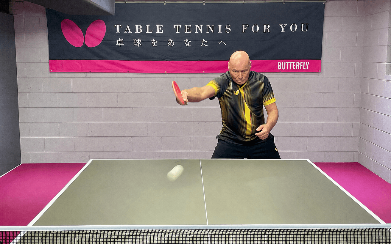 Coach Meinhard hitting a ping pong ball. Butterfly banner in the back - "Table Tennis for You"