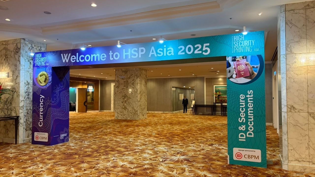 Conference entrance with a large banner reading "Welcome to HSP Asia 2025," featuring themes of high security printing, currency, and ID & secure documents, held in a hotel lobby with marble walls and patterned carpet.
