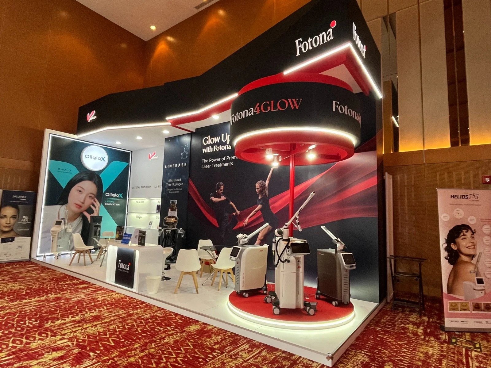 Booth display at a trade show showcasing Fotona laser treatments and devices, with promotional posters and seating area.