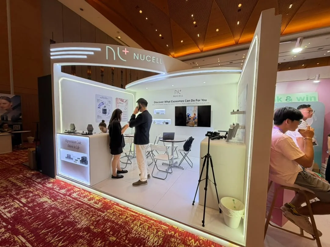 Exhibitor booth for Nucell featuring promotional materials, a video screen, and a conversation between two people at a conference or trade show.