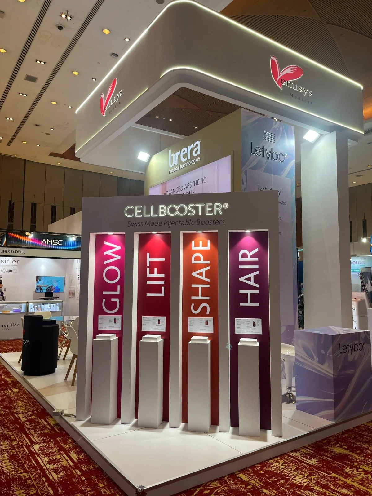 Exhibit display promoting Swiss-made injectable boosters with categories Glow, Lift, Shape, Hair, illuminated signs in an indoor convention center.
