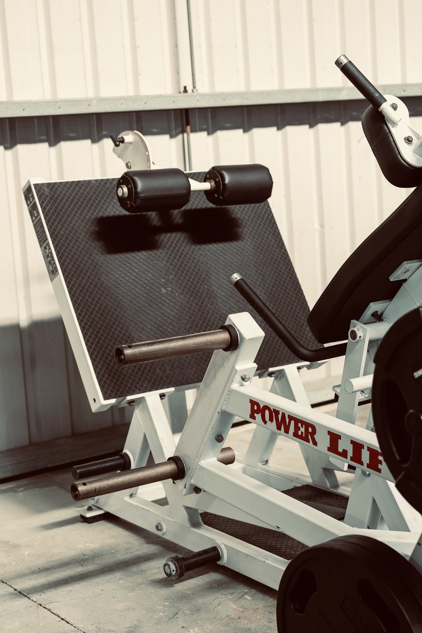 Outdoor gym equipment with weights and black rubber rollers, and a white metal frame with red text reading 'POWER LIFE'.