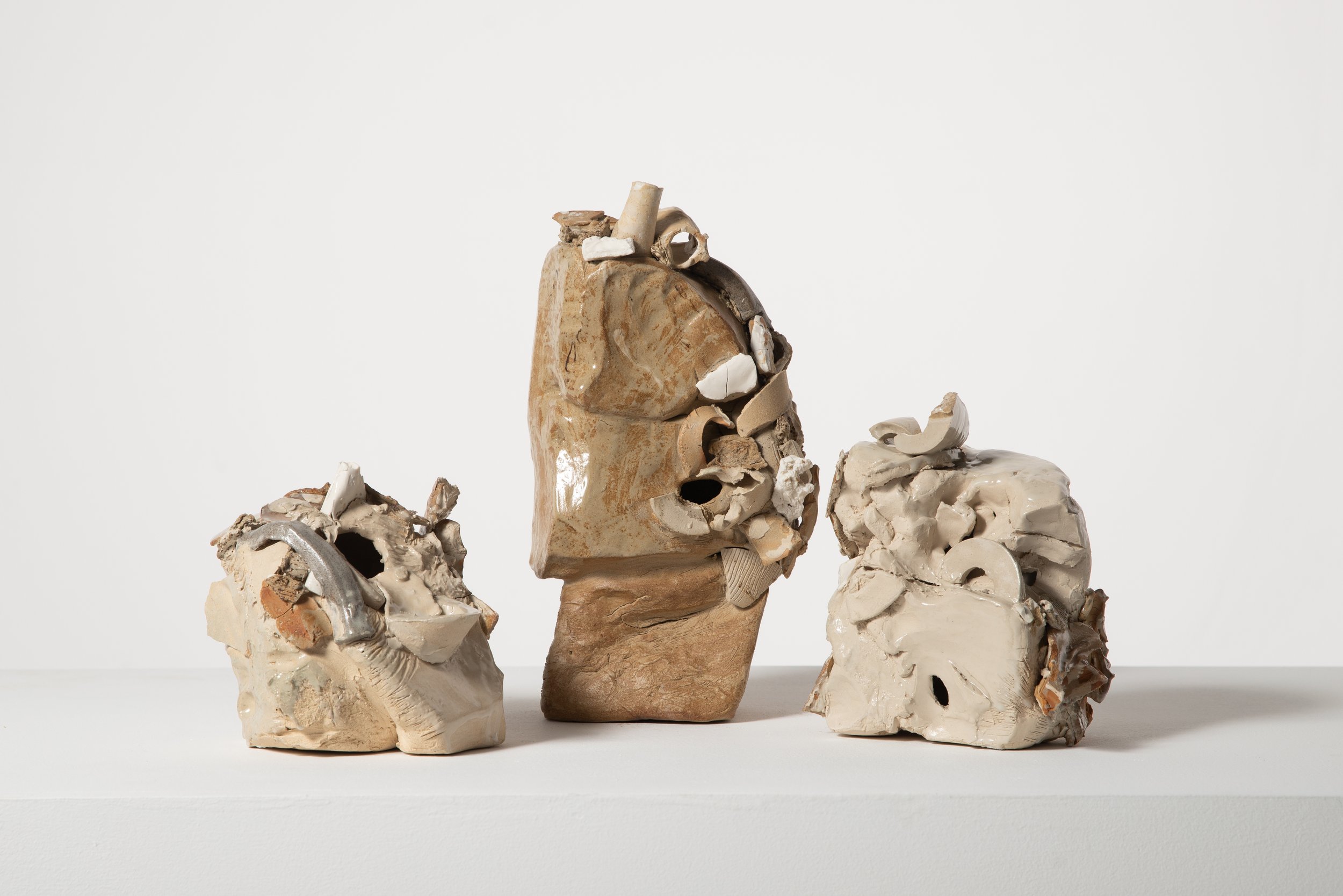 Abstract sculptures made from broken pottery and ceramic fragments arranged on a flat surface against a white background.