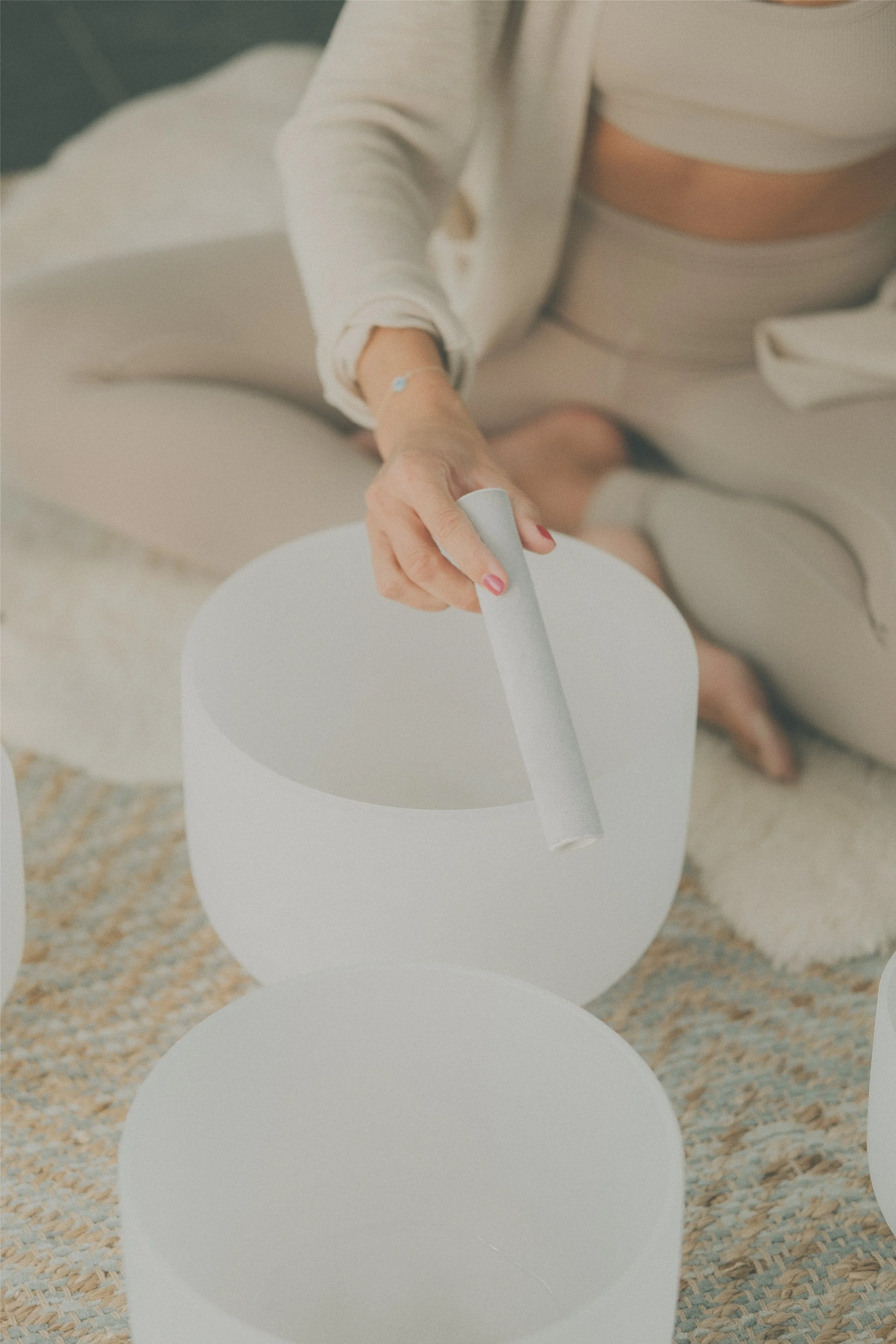Person seated playing a crystal singing bowl with a mallet