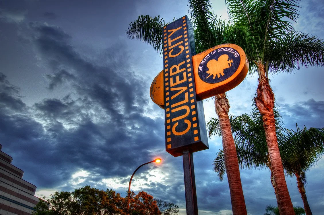 Sign for the University of Southern California (USC) with palm trees and a cloudy sky in the background