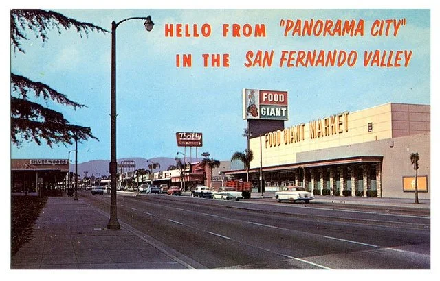 Vintage postcard of a street in San Fernando Valley, California, with a large sign reading "Hello from 'Panorama City' in the San Fernando Valley." The street has cars and storefronts, including a Food Giant supermarket.