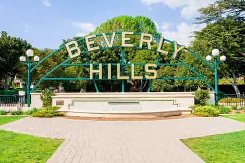 Beverly Hills sign in a park with trees and greenery in the background.