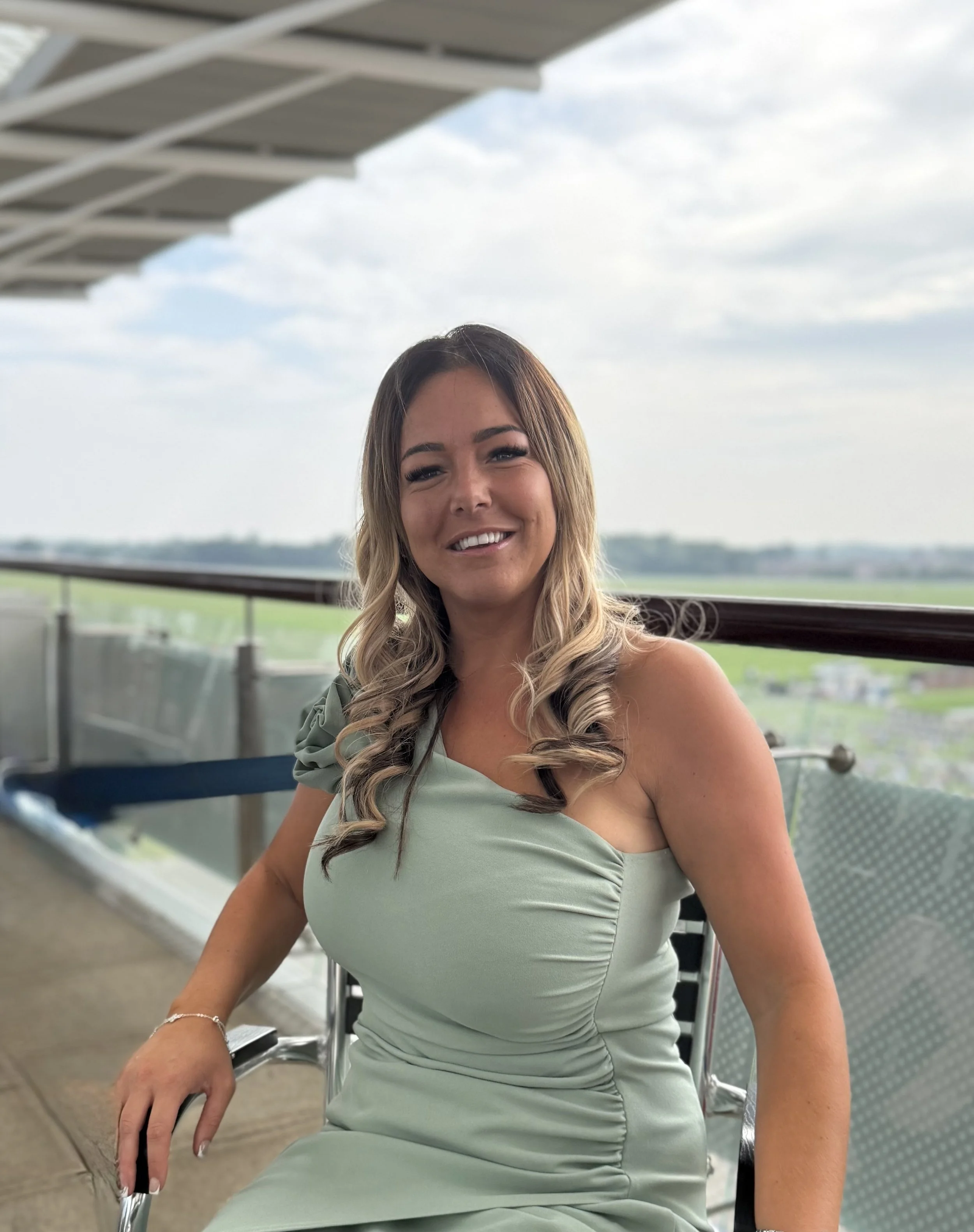 Female standing in garden smiling at camera,  with dark grey hair, wearing a black and white patterned top