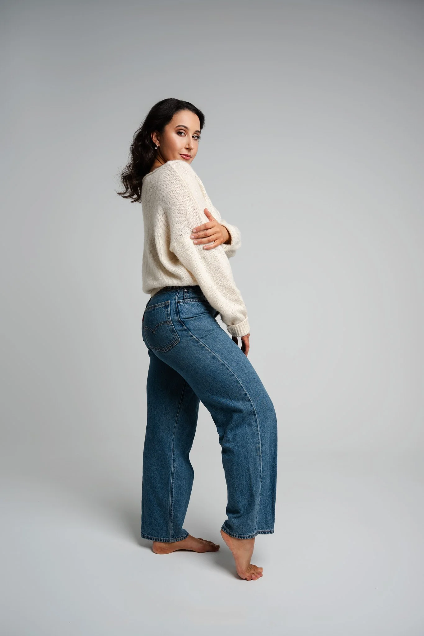 a model in blue jeans and a white jumper standing on the side