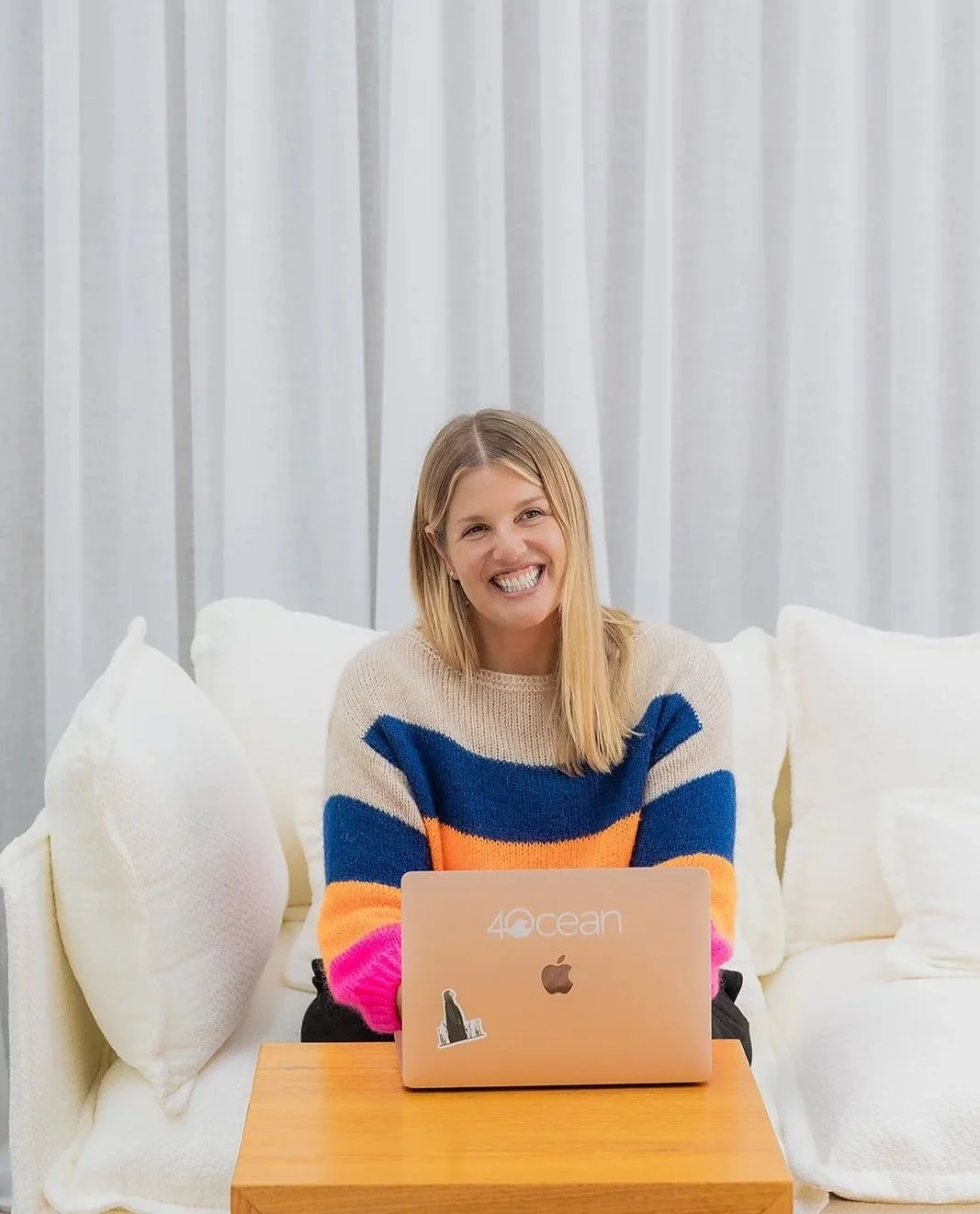 an image of a woman smiling sitting on a white couch with her laptop in front of her