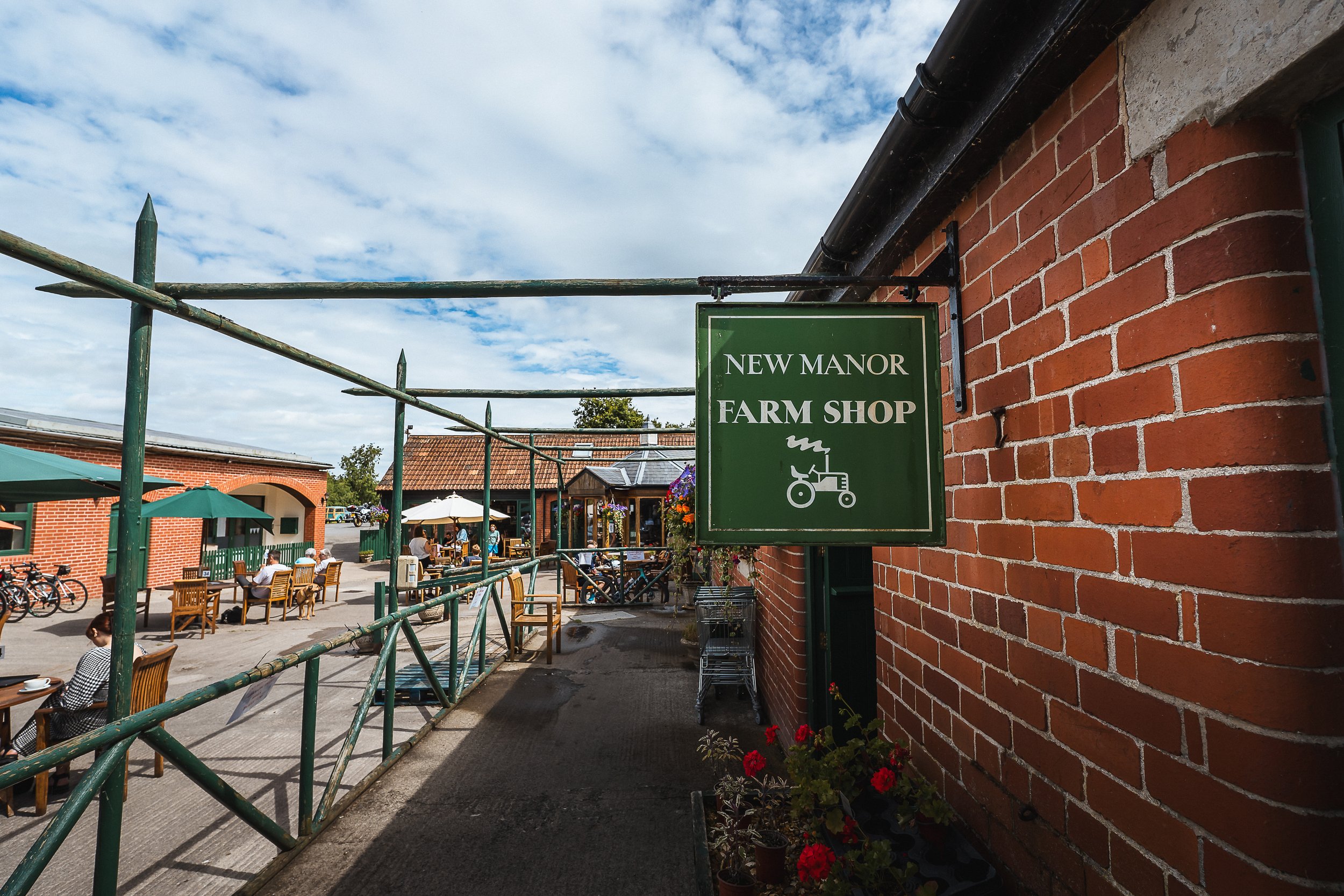 Entrance to New Manor Farm Shop with outdoor seating and green sign on a brick wall.