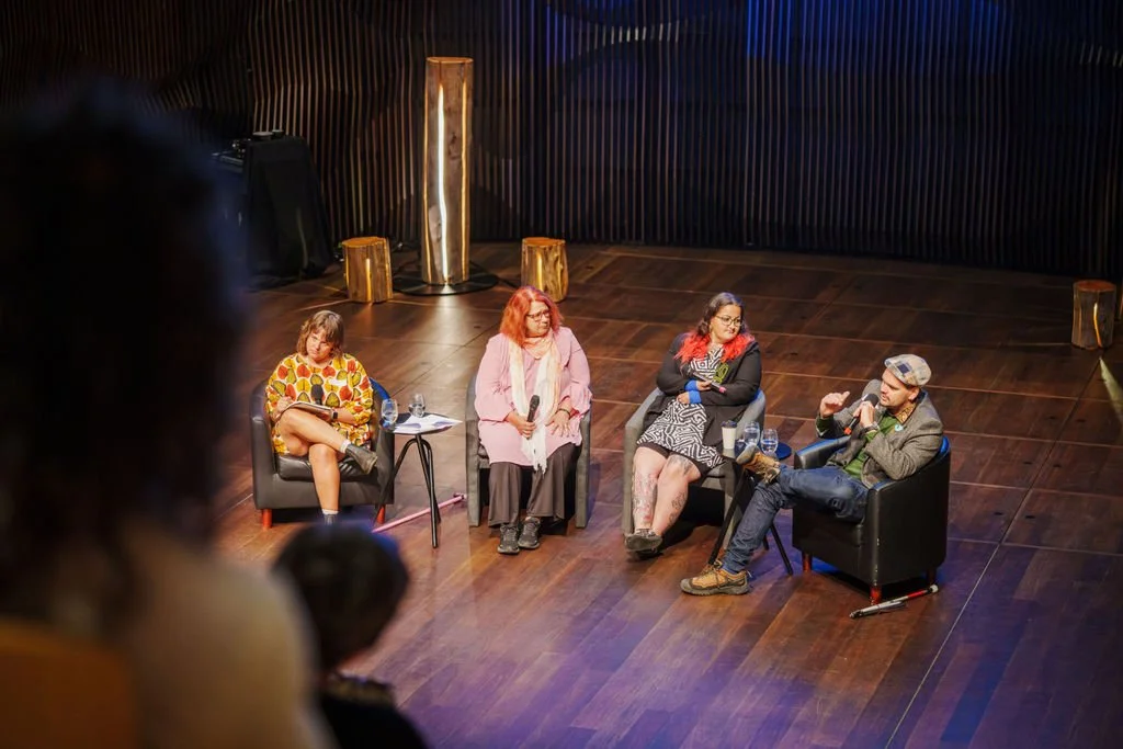 A panel discussion on stage with four people. The man on the far right is speaking into a microphone.