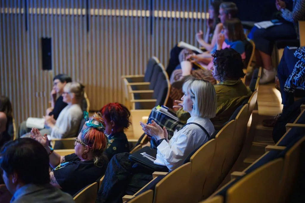 Audience members sitting in the tiered seated auditorium applaud.