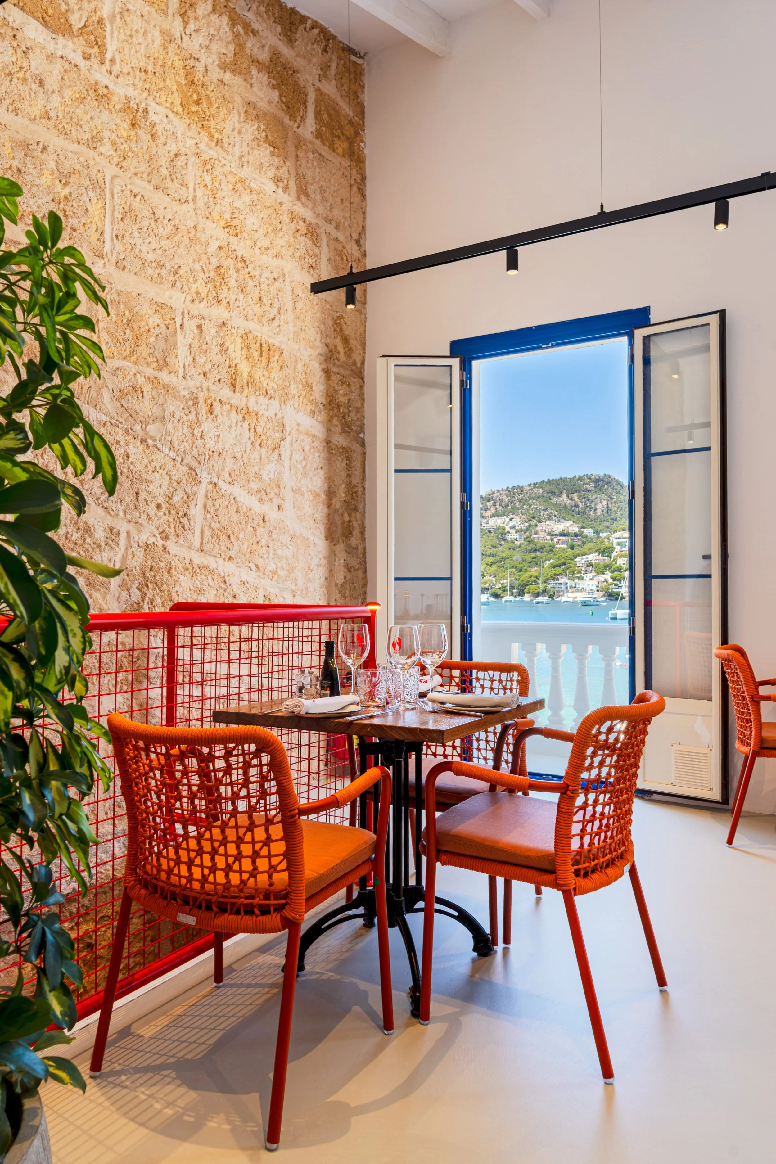Mesa en un restaurante con platos, cubiertos y copas, junto a una ventana con vista a un mar y colinas.