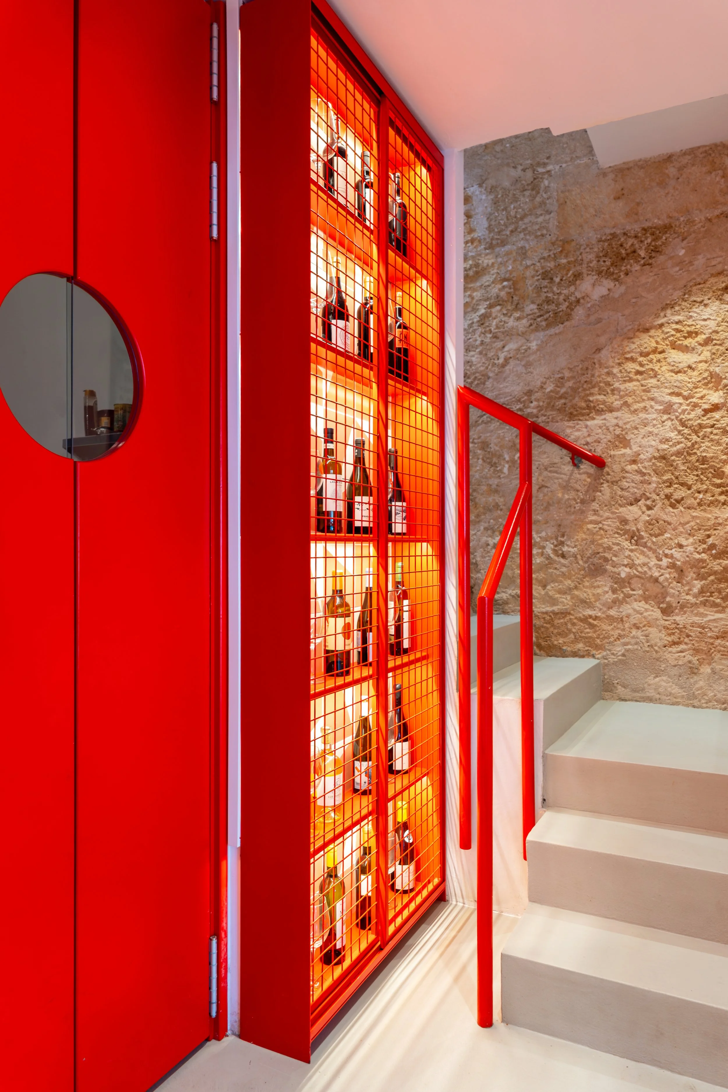 Estante de metal roja con botellas de vino en una pared de piedra en un espacio interior moderno