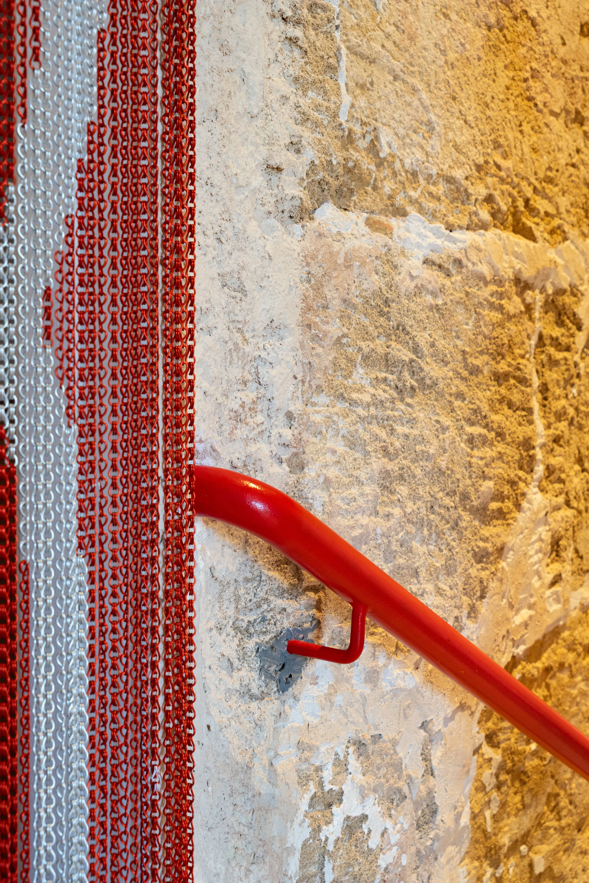 Pasamanos de escaleras en color rojo junto a una pared de piedra