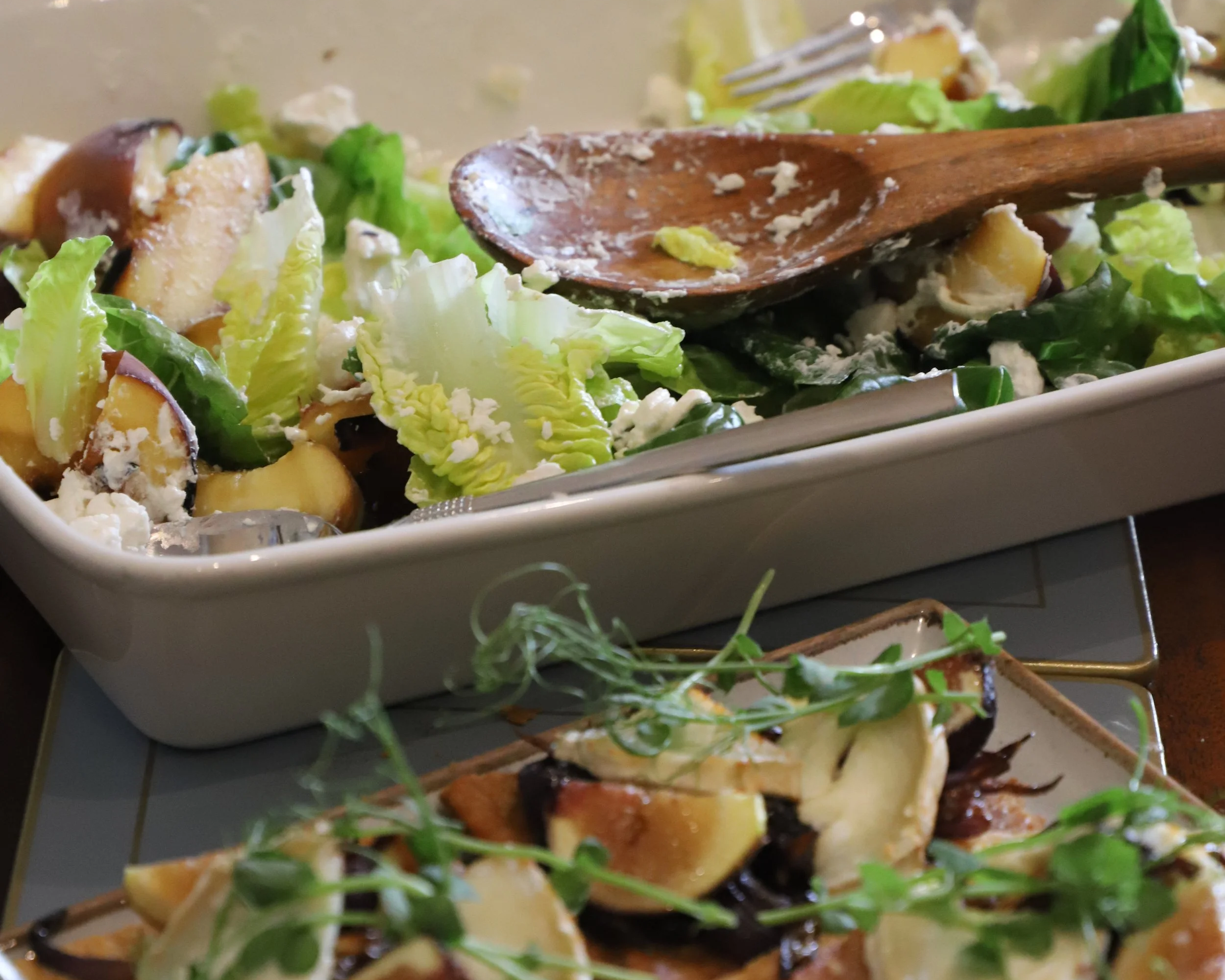 Close-up of a dish with mixed greens, roasted potatoes, grilled chicken, and garnished with microgreens on a white serving platter.