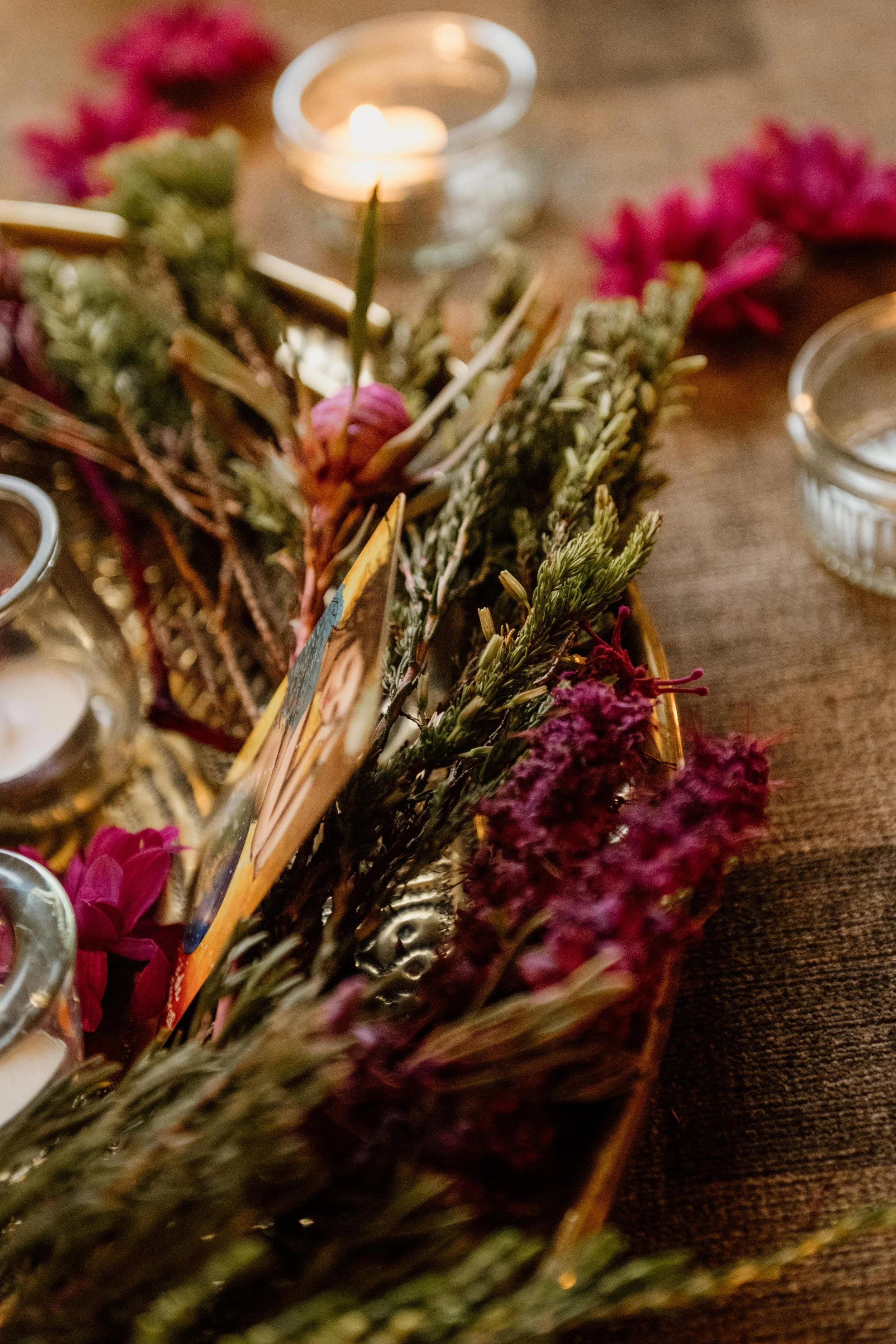 Close-up of a wreath with dried lavender and pink flowers, surrounded by small candles, on a wooden surface.