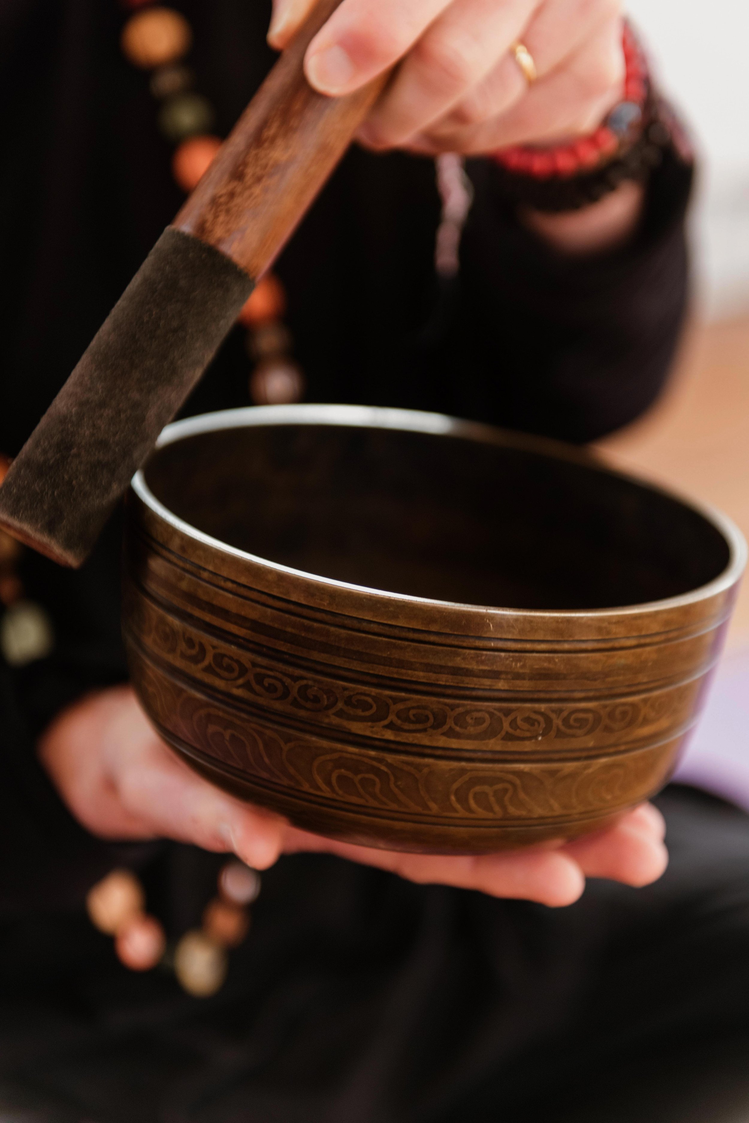 Person holding a wooden singing bowl with a mallet, wearing beaded bracelets and a black outfit.