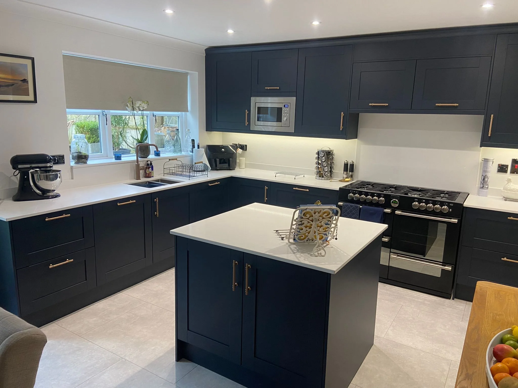 Modern kitchen corner with white cabinets, electric stovetop, kettle, countertop decor, window view, and sink.