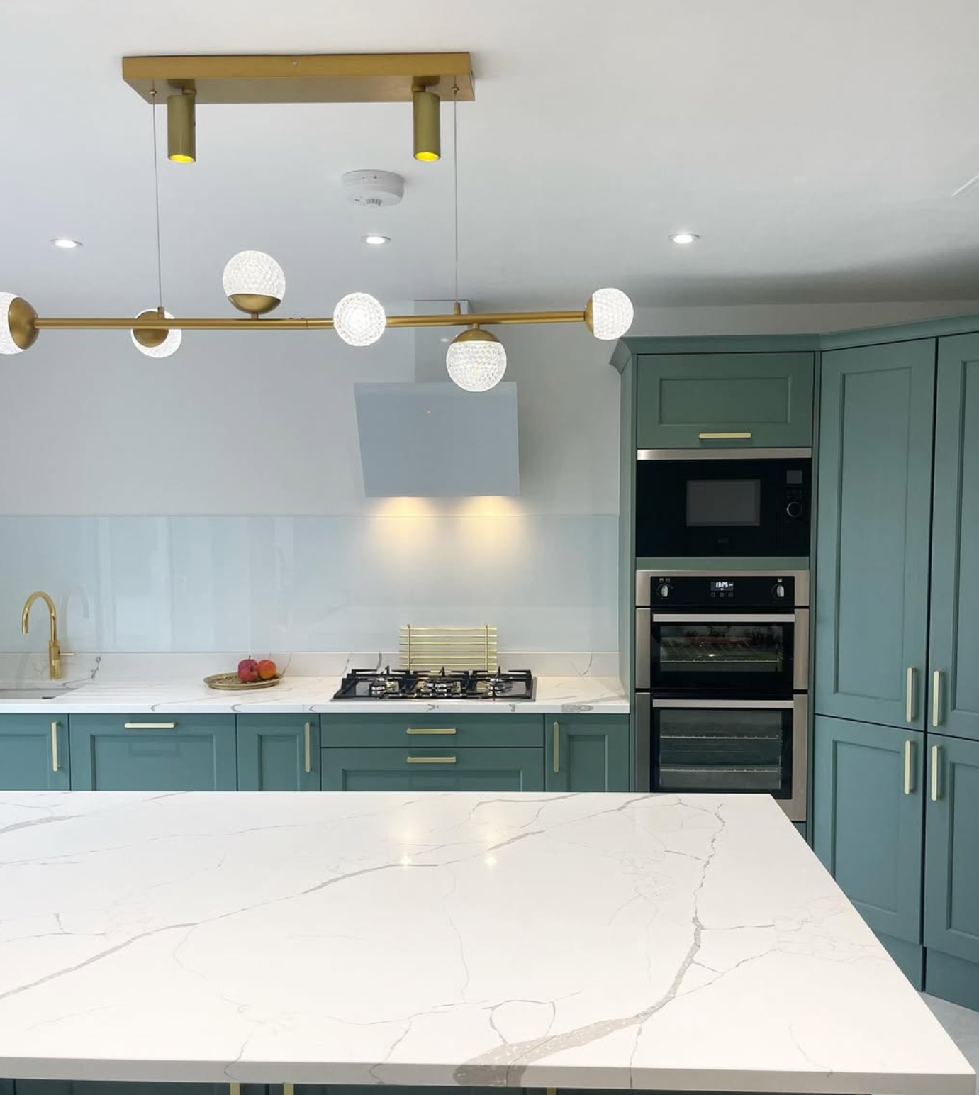Modern kitchen corner with white cabinets, electric stovetop, kettle, countertop decor, window view, and sink.