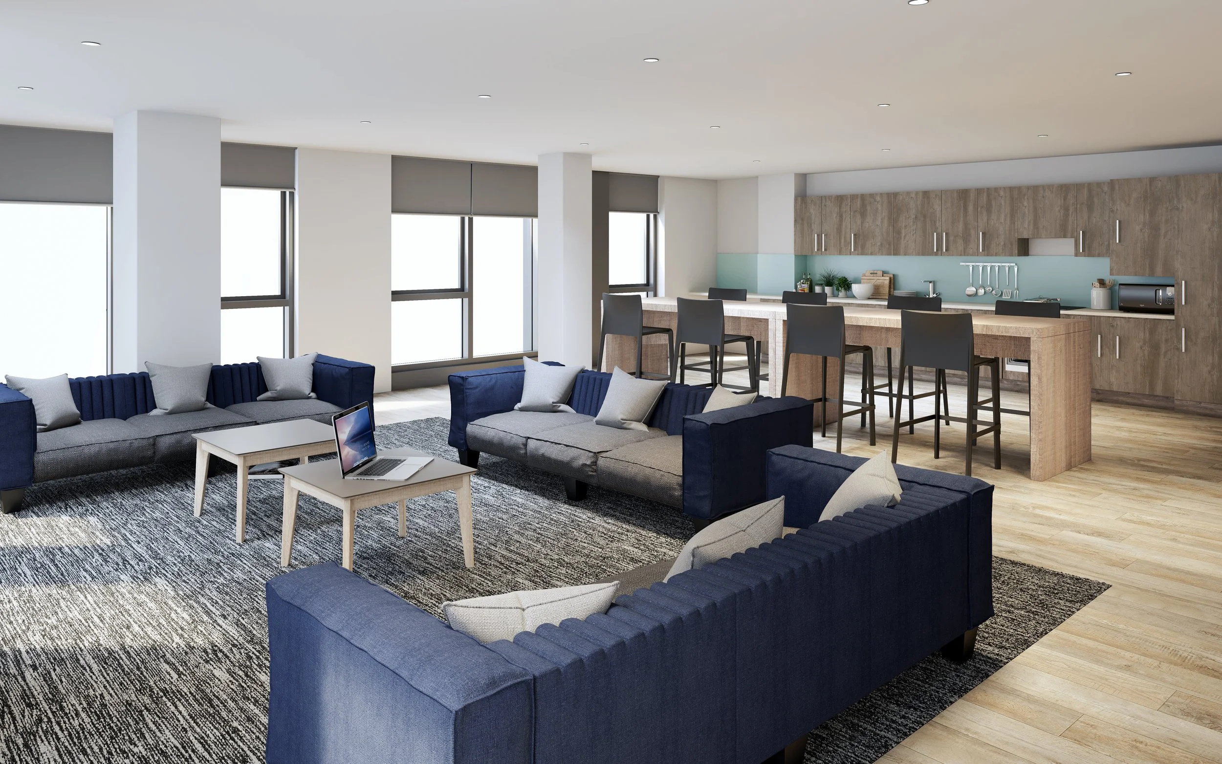 Modern open-concept living room and kitchen with blue sofas, gray pillows, a laptop on a coffee table, bar stools at a kitchen island, and wooden cabinetry.
