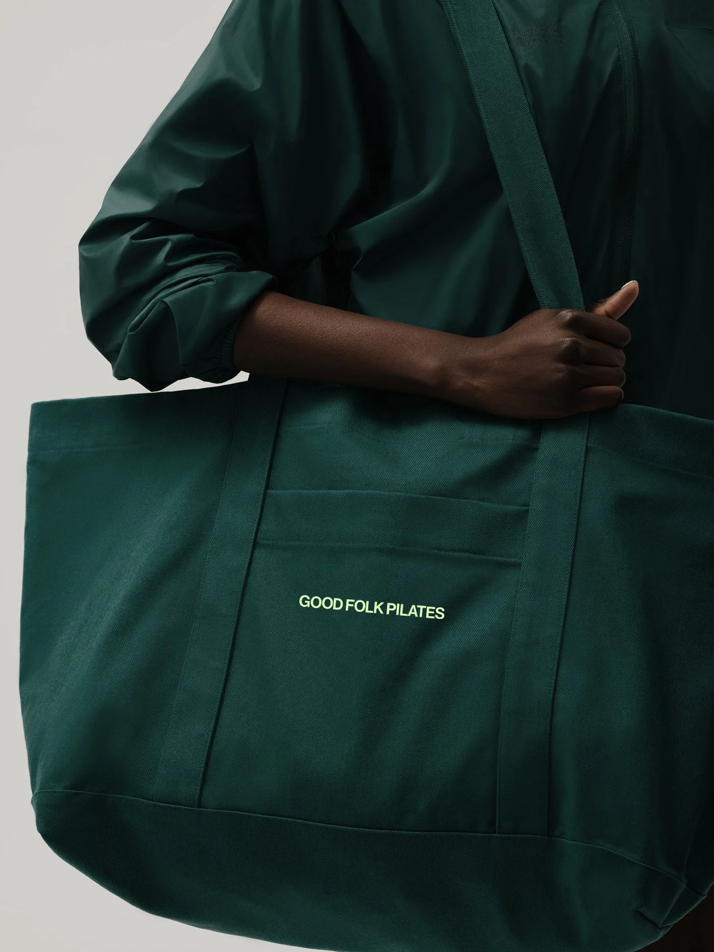 A green tote bag with white text that reads "Good Folk Pilates" on the front.