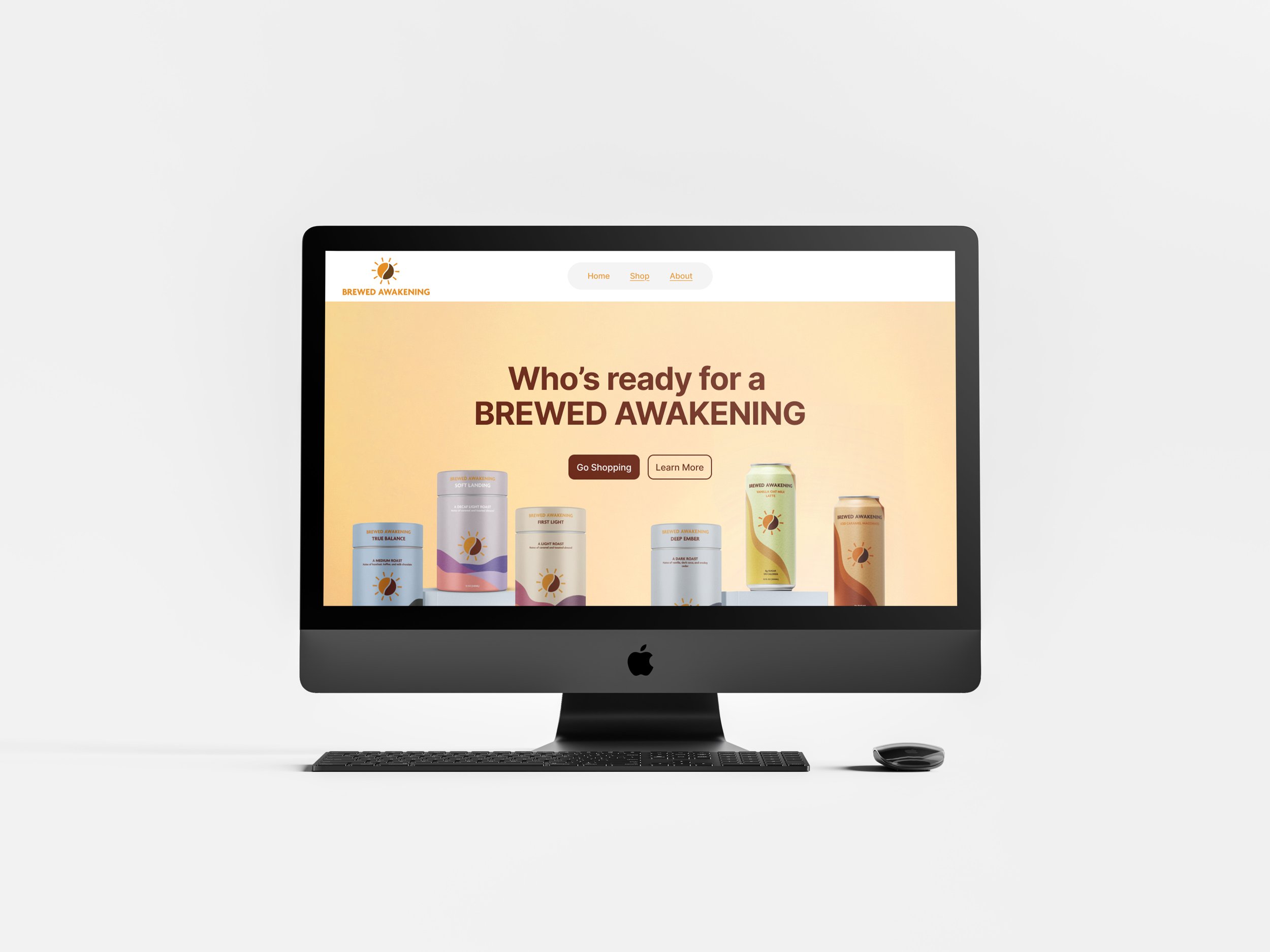 An Apple iMac computer with a keyboard and mouse displays a website for Brewed Awakening coffee. The website's header has a logo, navigation menu with links to Home, Shop, and About, and a main section with the text "Who's ready for a BREWED AWAKENING" and images of canned coffee products.
