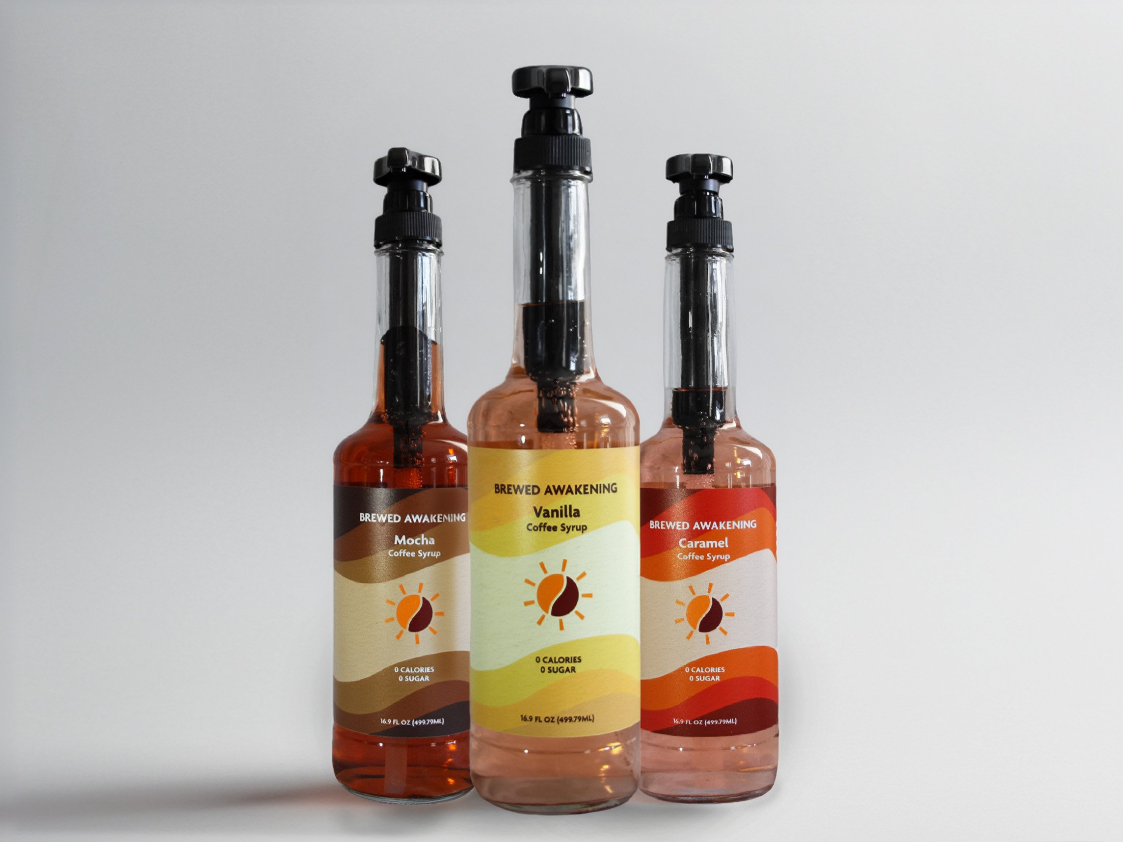 Three bottles of coffee syrup with black pump dispensers, labeled as Mocha, Vanilla, and Caramel, with a light-colored background.