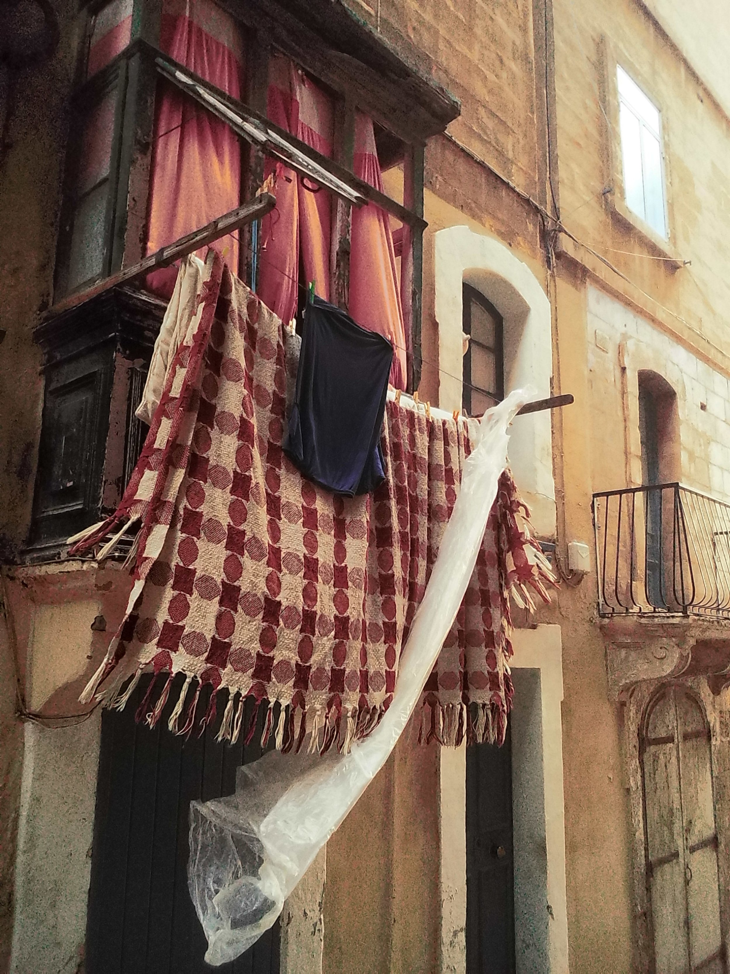 Clothes hanging on a clothesline outside an old, yellow building with small balconies and arched windows.