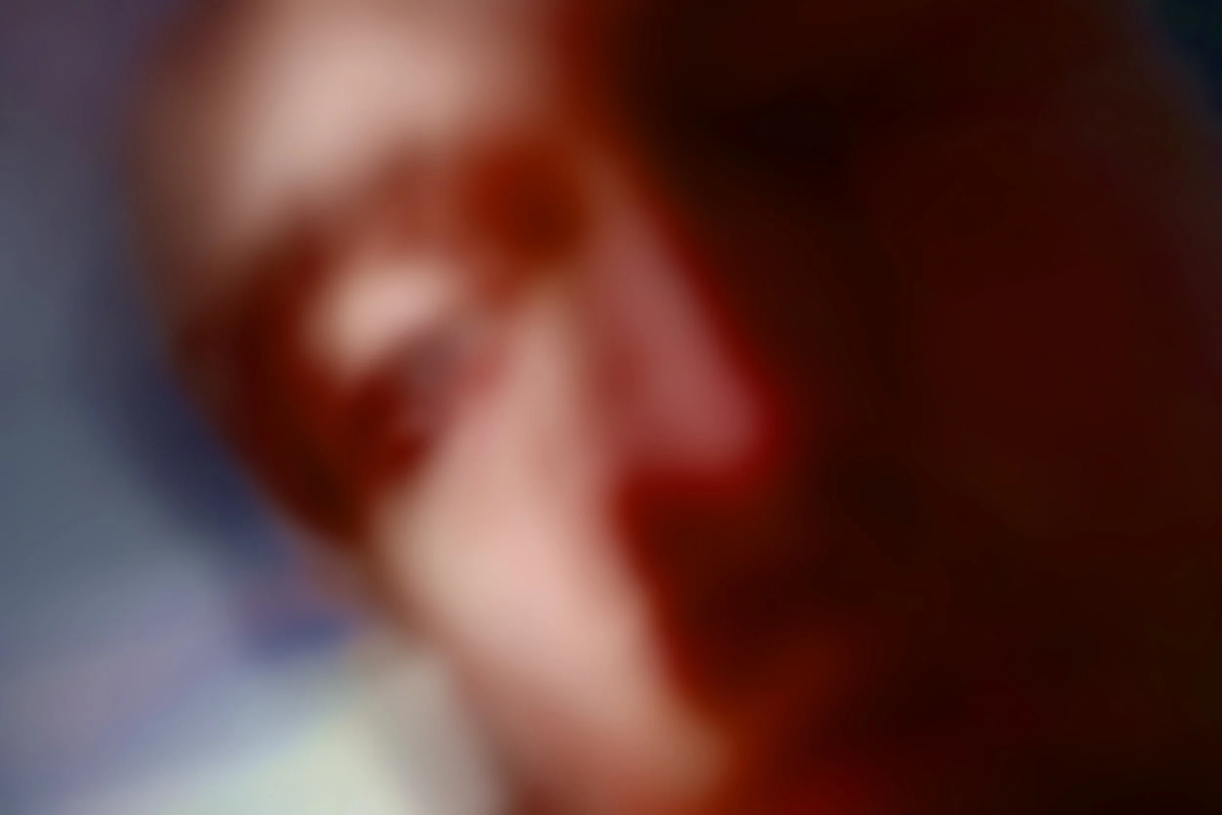 A heavily blurred, close-up image of a person's face, making details indistinguishable.