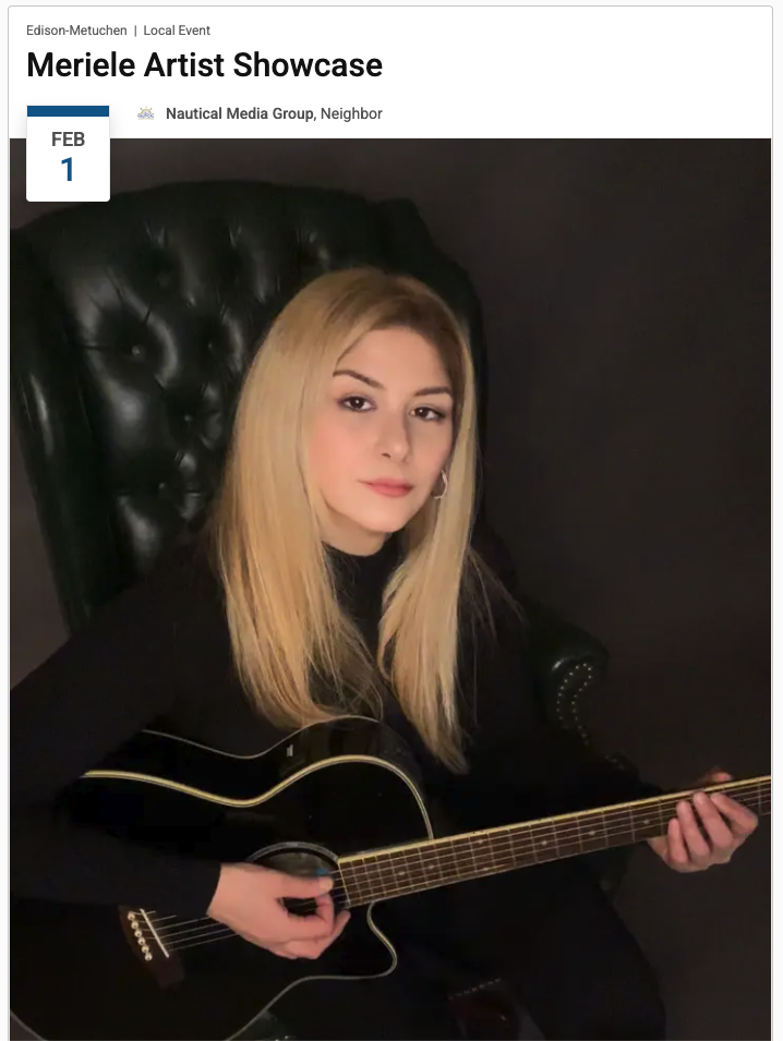 American singer-songwriter Meriele with long blonde hair sitting in a black leather armchair, holding and playing a black acoustic guitar. The background is dark, and she is wearing a black top, looking directly at the camera.