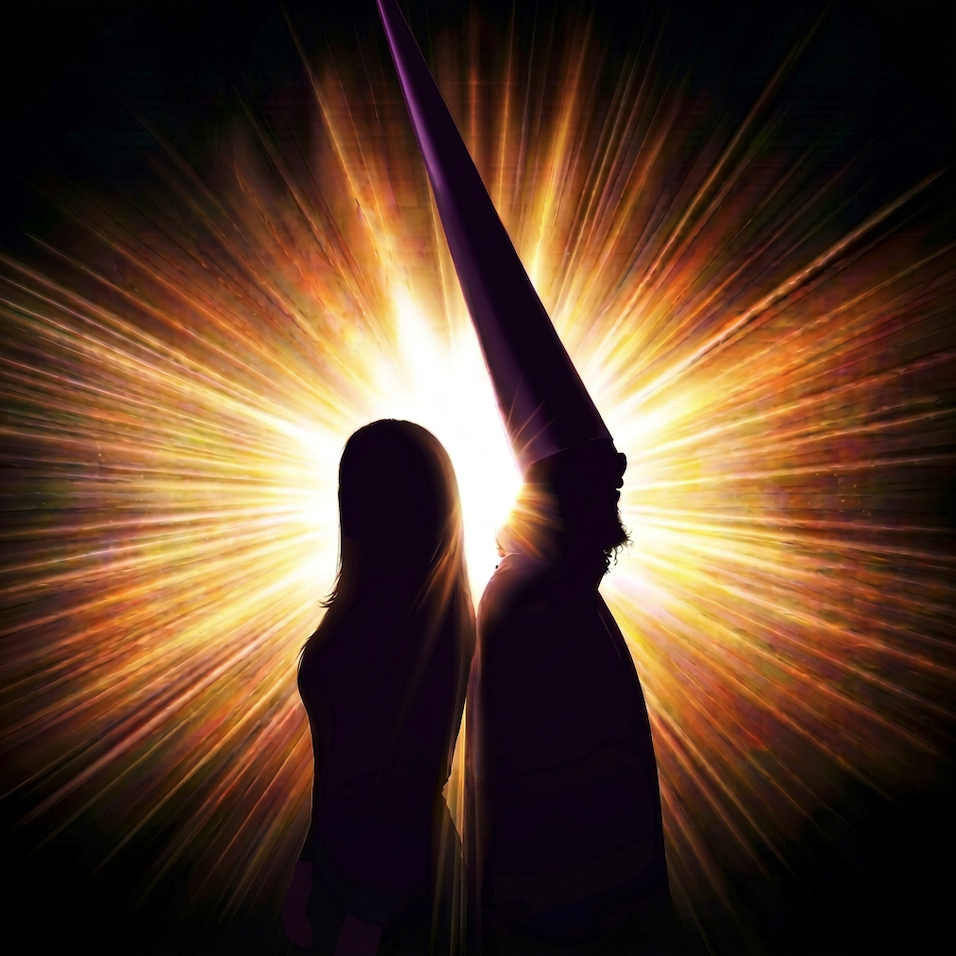 Silhouettes of a woman and a man wearing a cone-shaped hat with a bright, radiant explosion of light behind them
