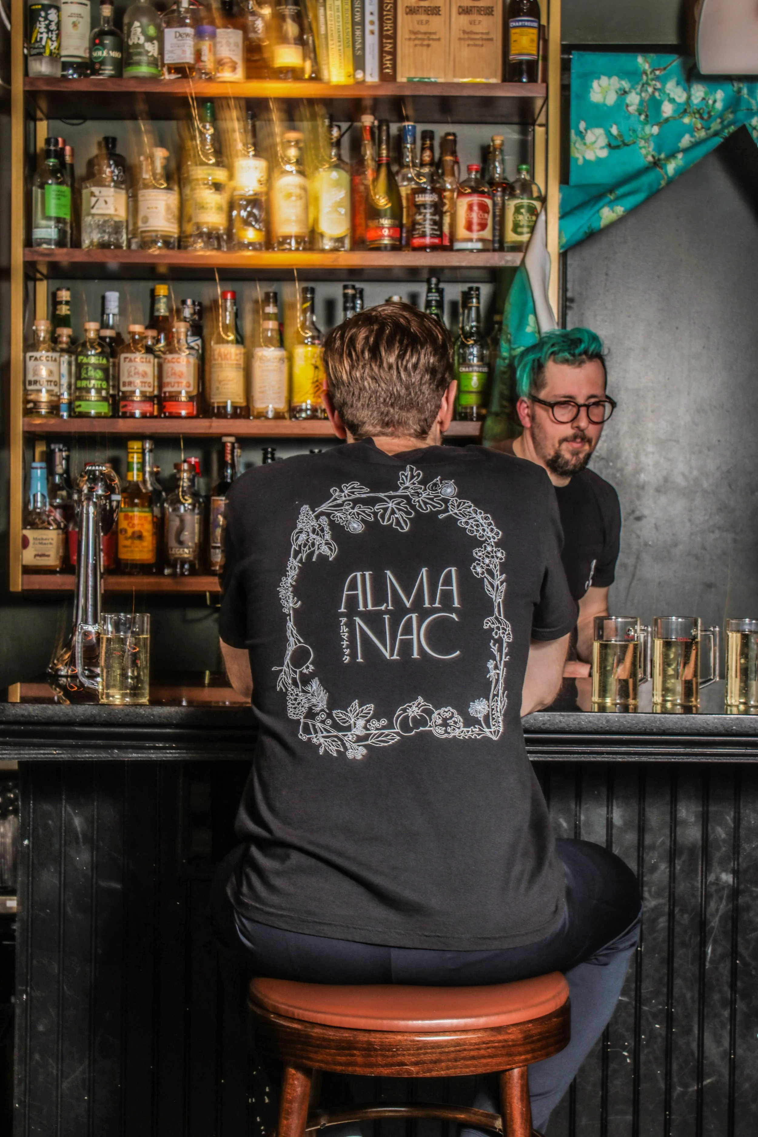 Back of black almanac t shirt, man sitting at bar