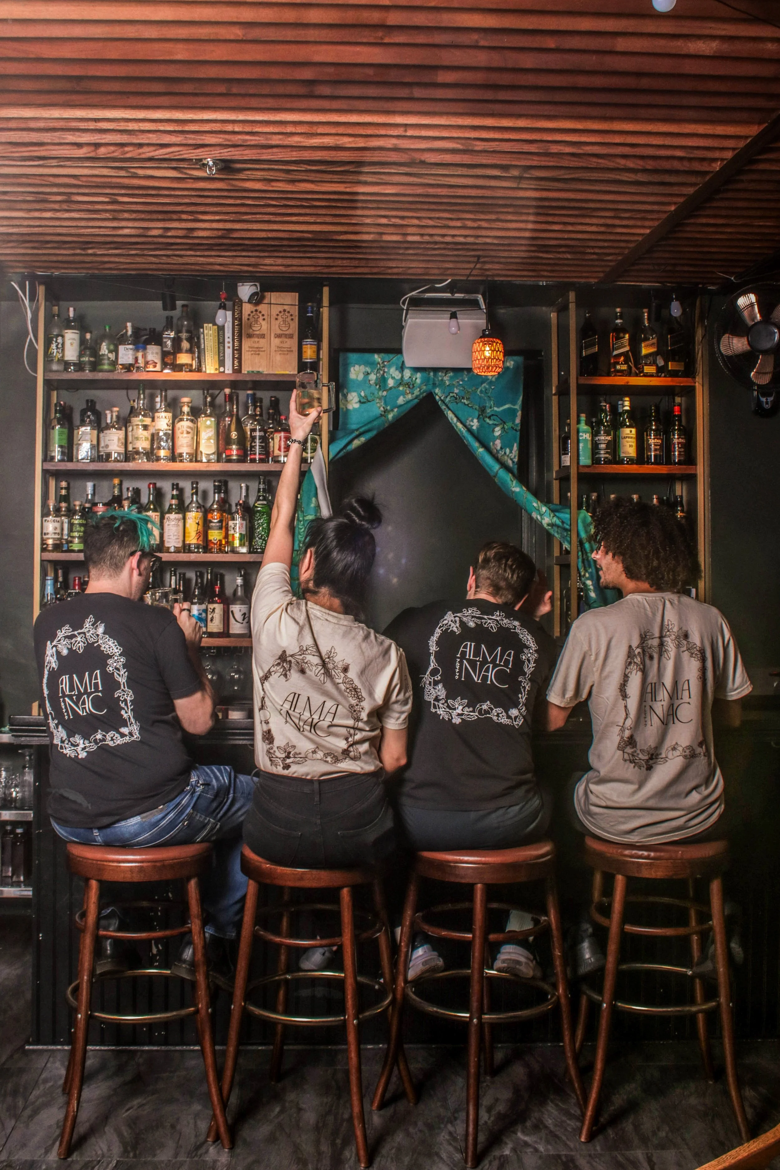 group of four sitting at almanac bar, all with back of tee shirt showing.